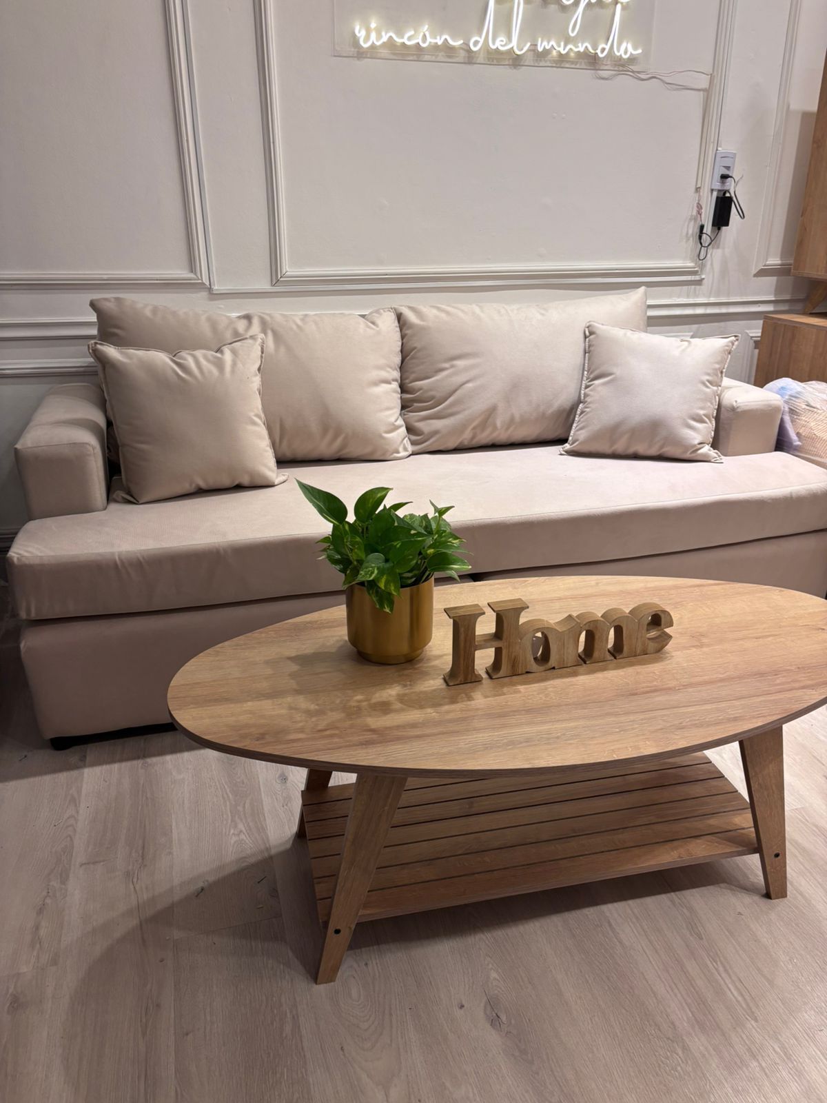 Sofá beige con almohadas, mesa de centro de madera, planta y cartel