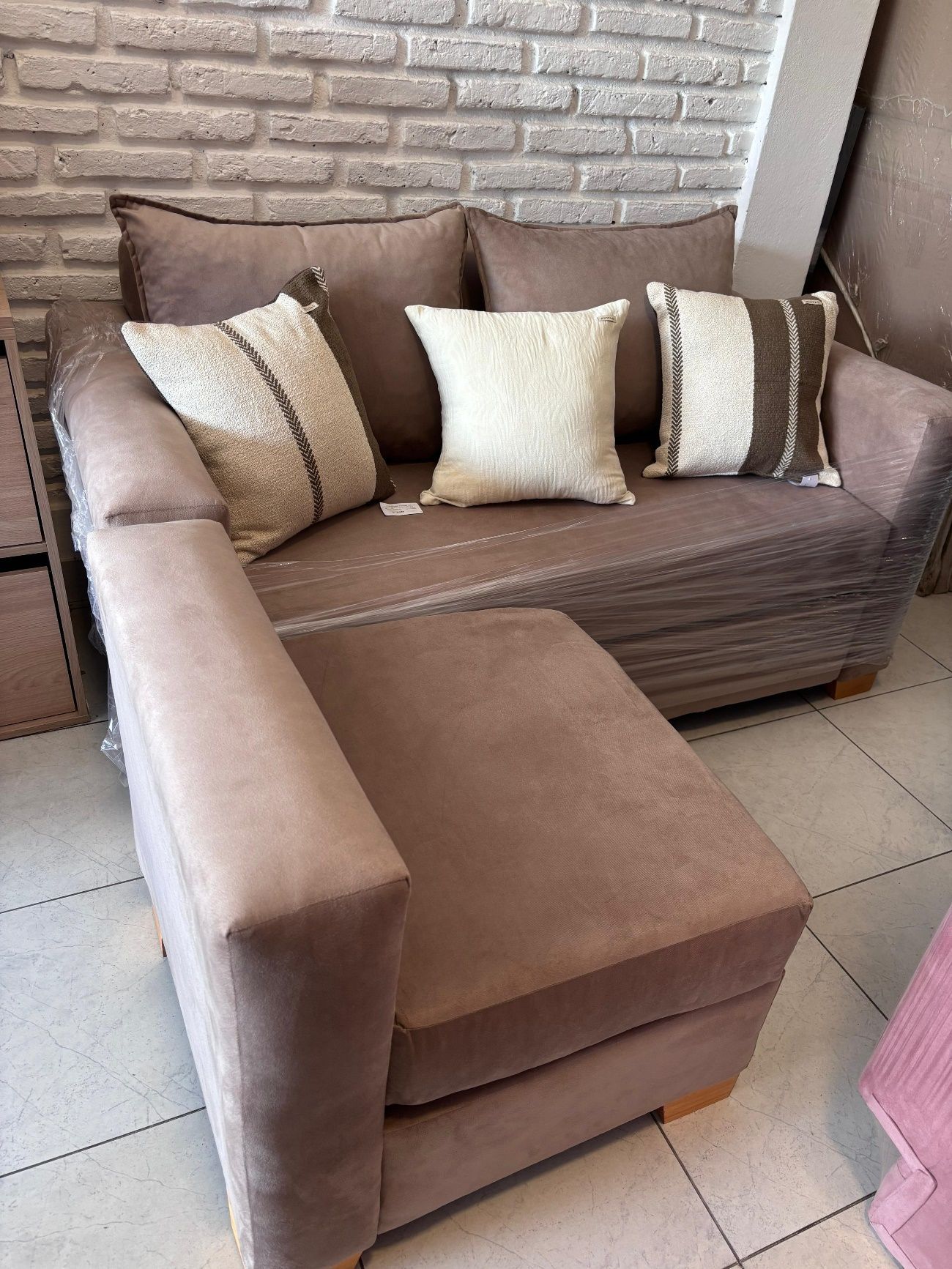 Sofá seccional marrón con almohadas contra una pared de ladrillos.