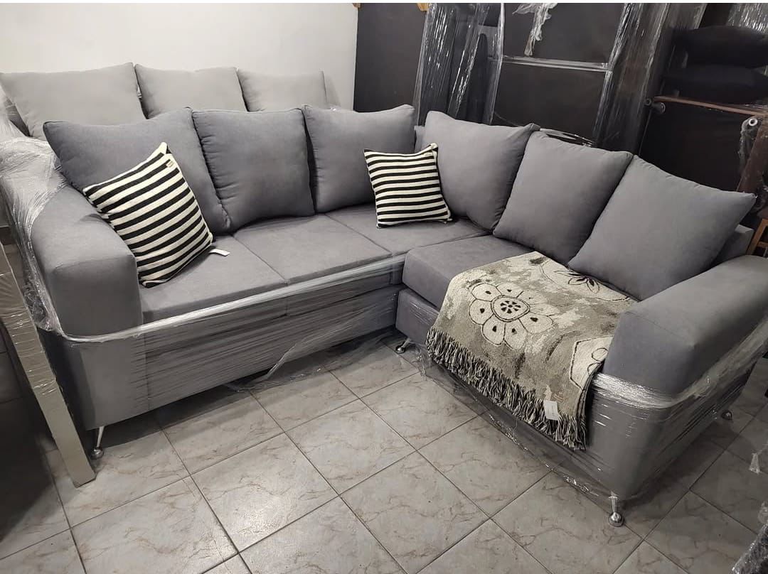 Sofá seccional gris con cojines y manta en una habitación.