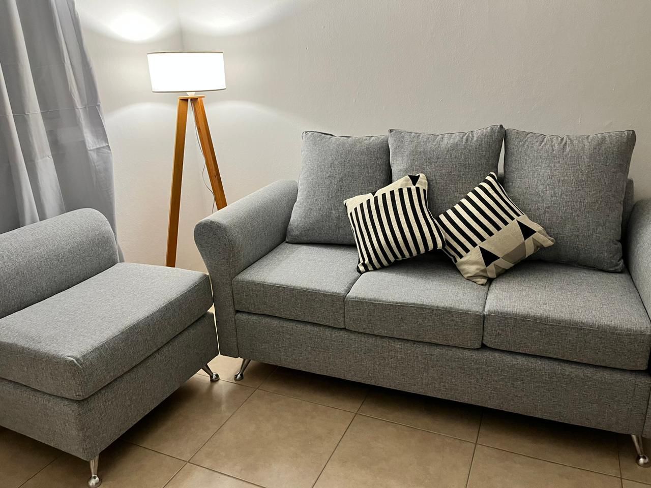 Conjunto de sofá y sillón gris con cojines, junto a una lámpara de pie de madera, en una habitación.