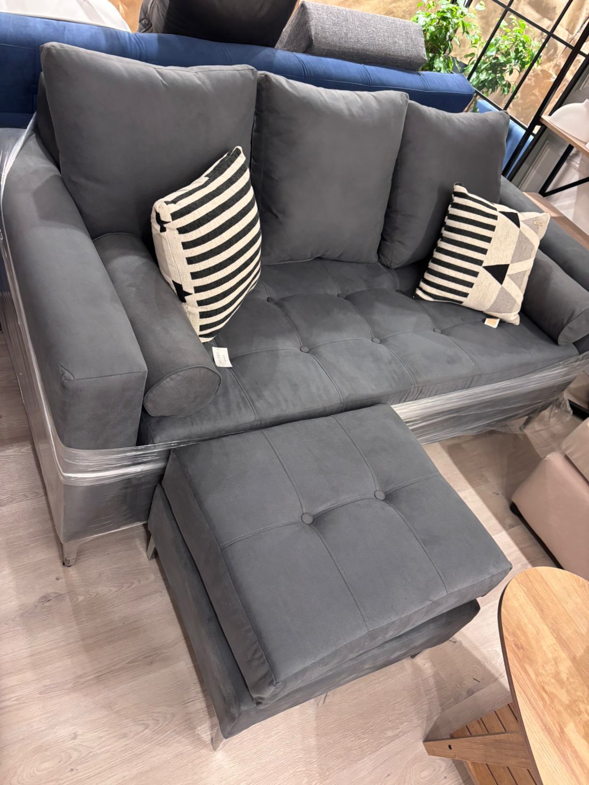 Sofá seccional gris con otomana y cojines a juego en una tienda.