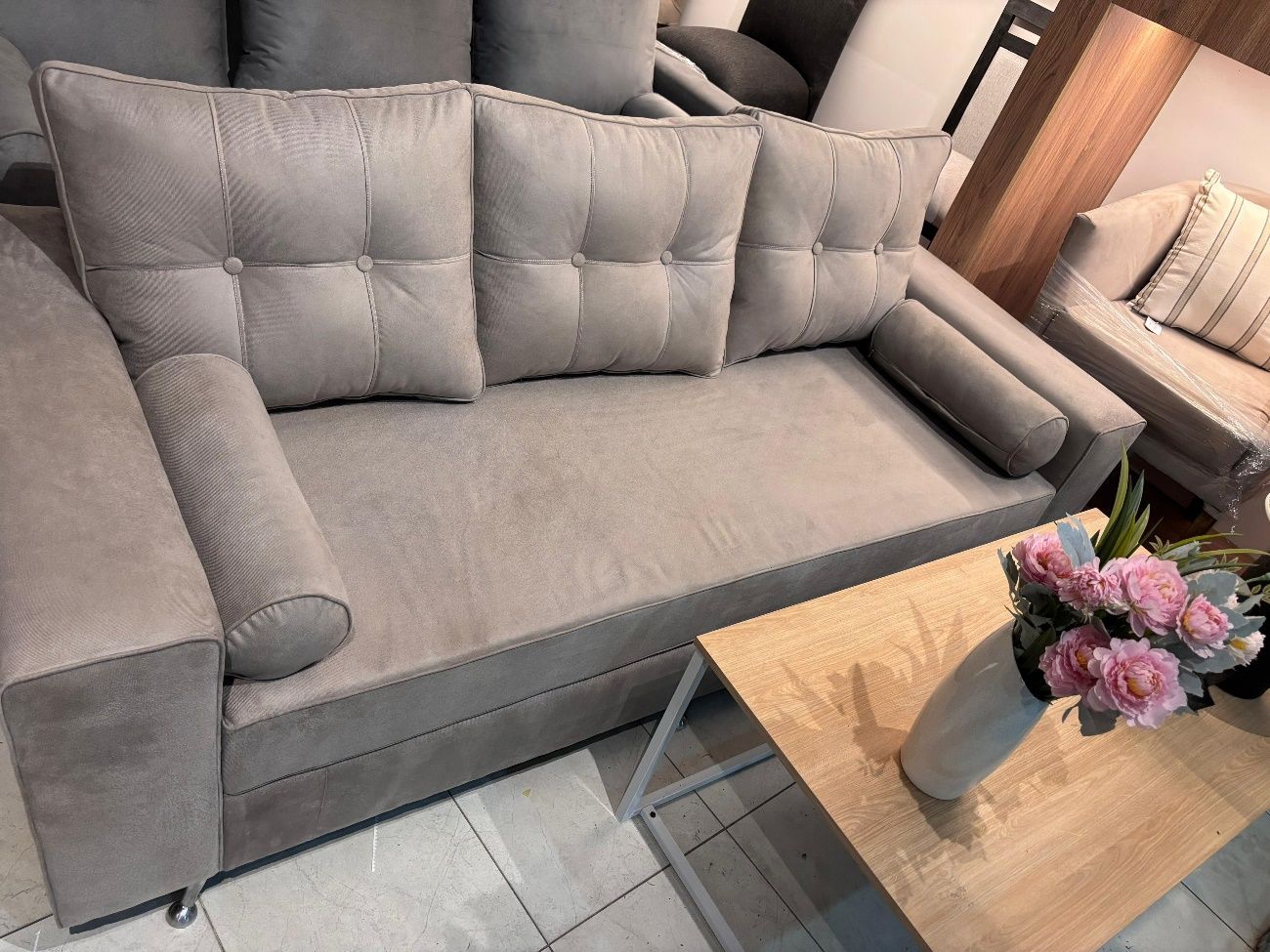 Sofá capitoné beige con cojines a juego, cerca de una mesa de café con flores.