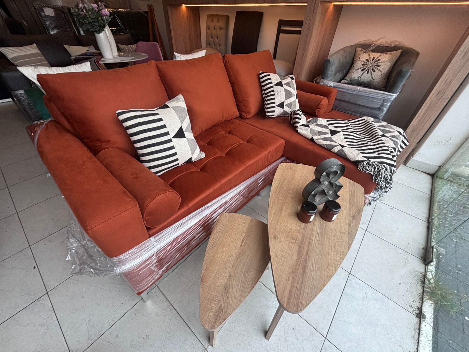 Sofá seccional naranja con almohadas decorativas, dos mesas auxiliares de madera y un sillón gris.