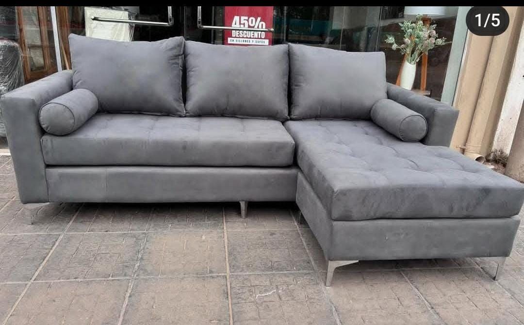 Sofá seccional gris con tres cojines de respaldo y chaise longue.