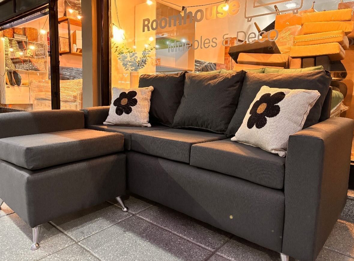 Sofá seccional gris oscuro con patas plateadas y almohadones con flores en una tienda.