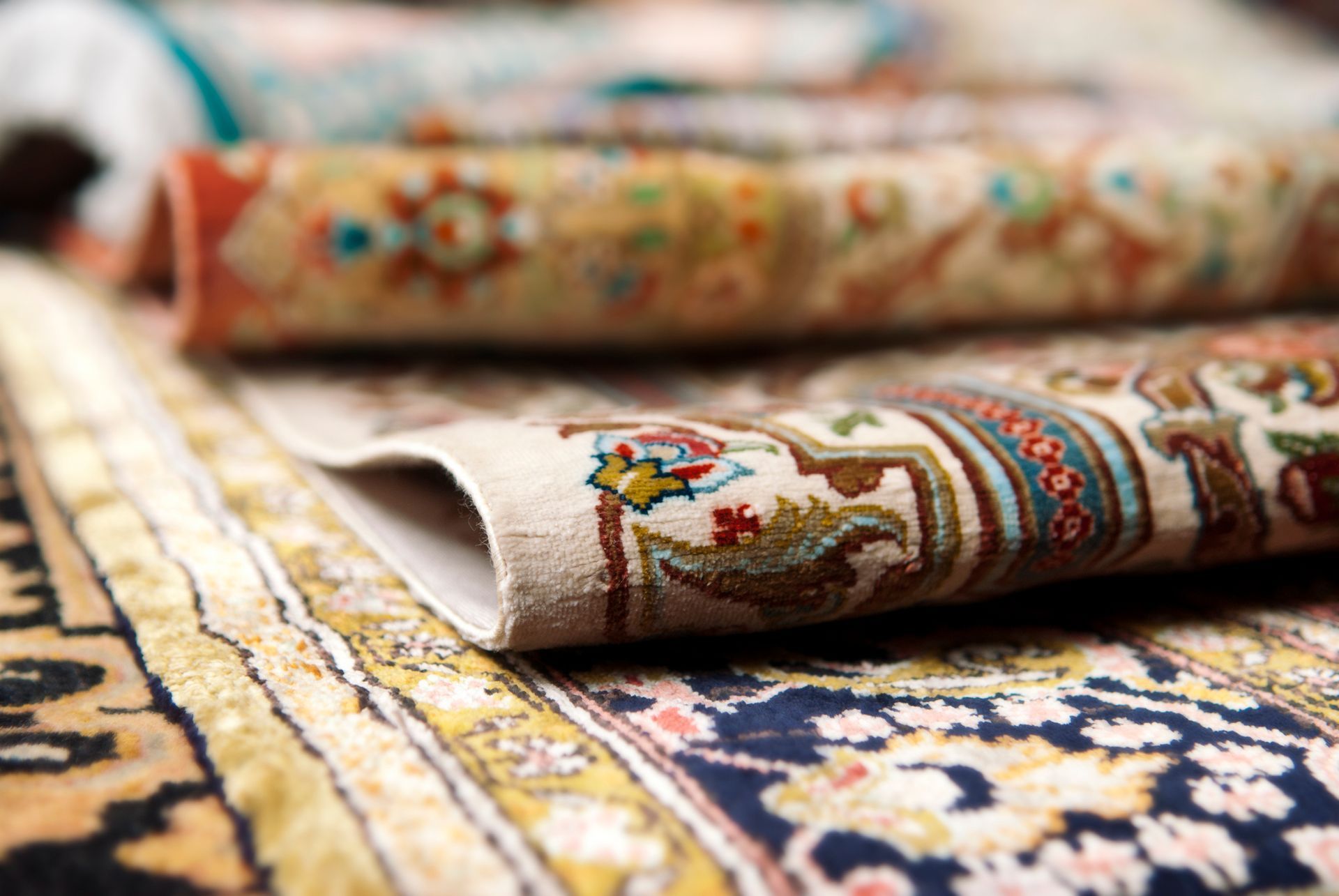 Rolled-up ornate rugs with colorful floral patterns, stacked on top of each other.