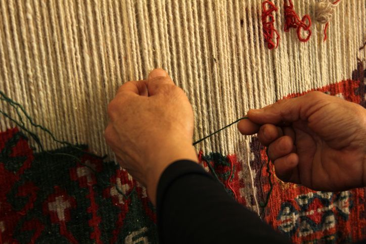 Hands weaving a rug, threading yarn into vertical strands.
