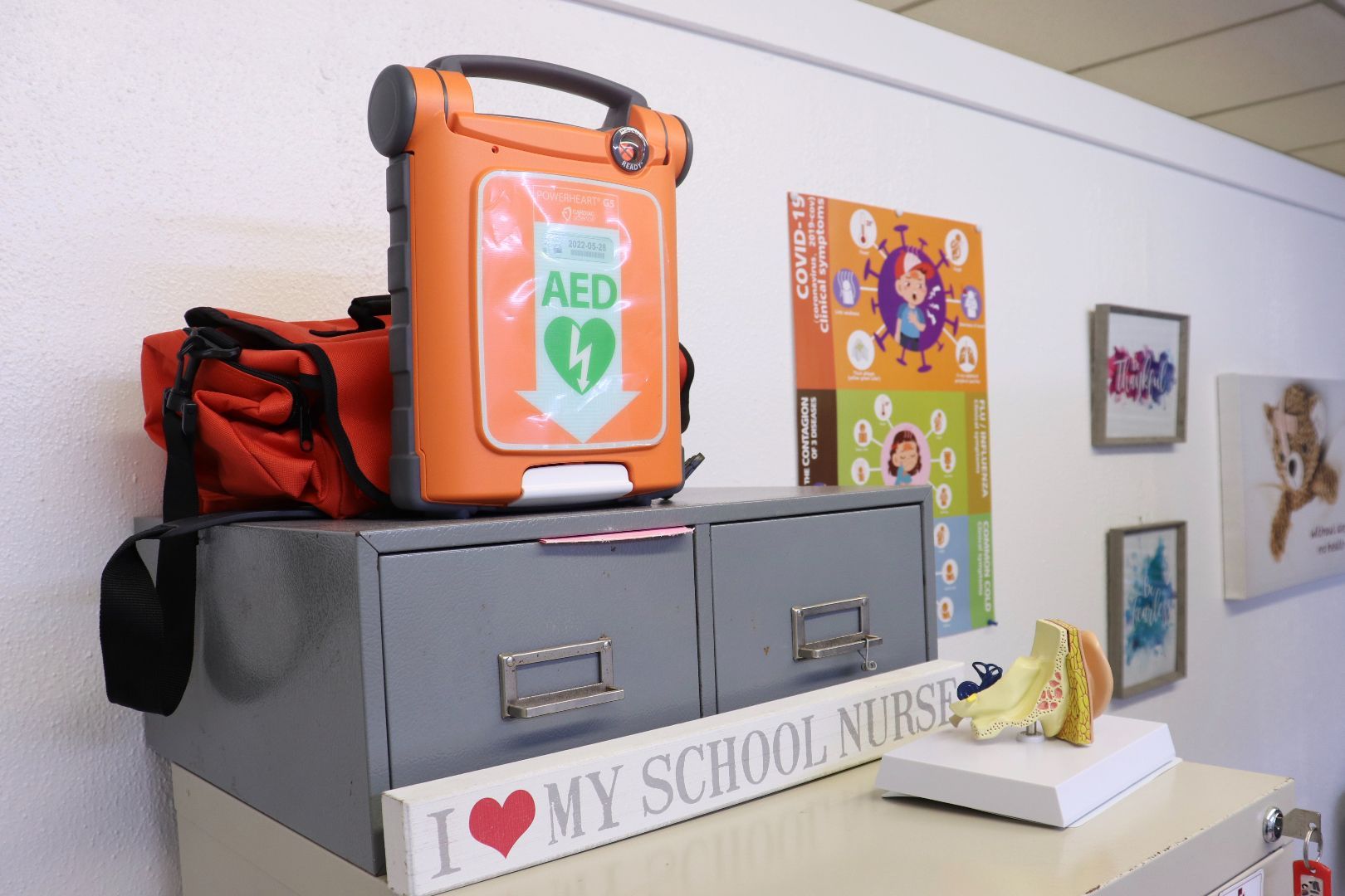 An aed device is sitting on top of a shelf next to a sign that says i love my school nurse