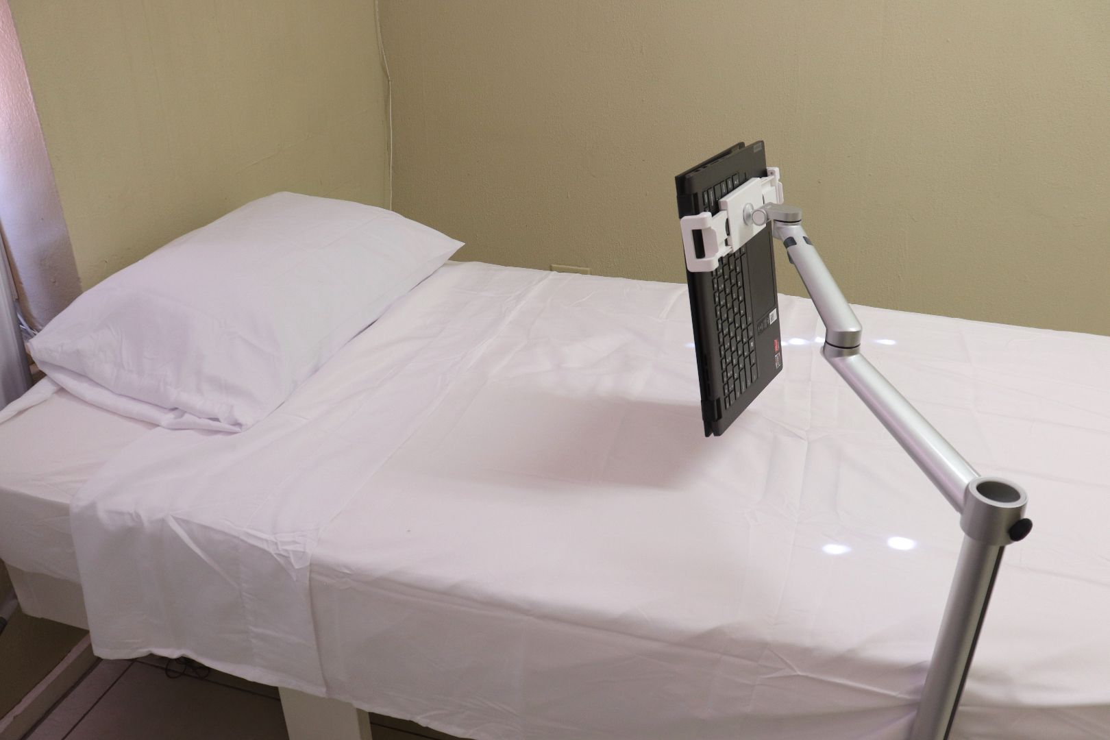 A bed with white sheets and a tablet on a stand