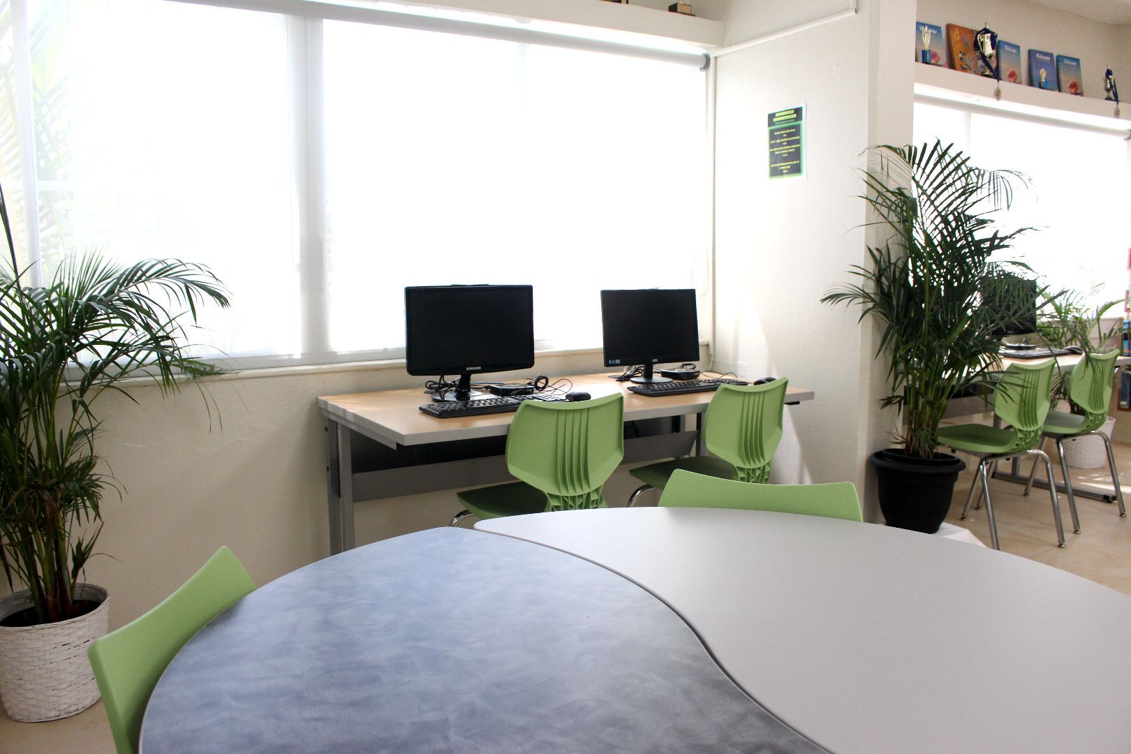 Two computer monitors sit on a desk in a room with green chairs