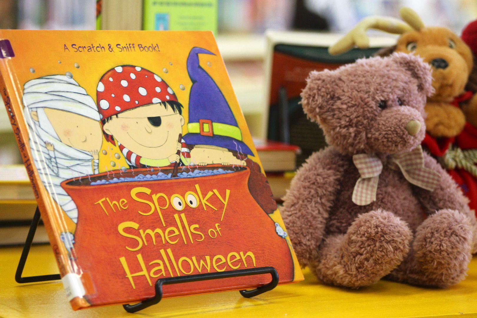 A teddy bear sits next to a book titled the spooky smells of halloween