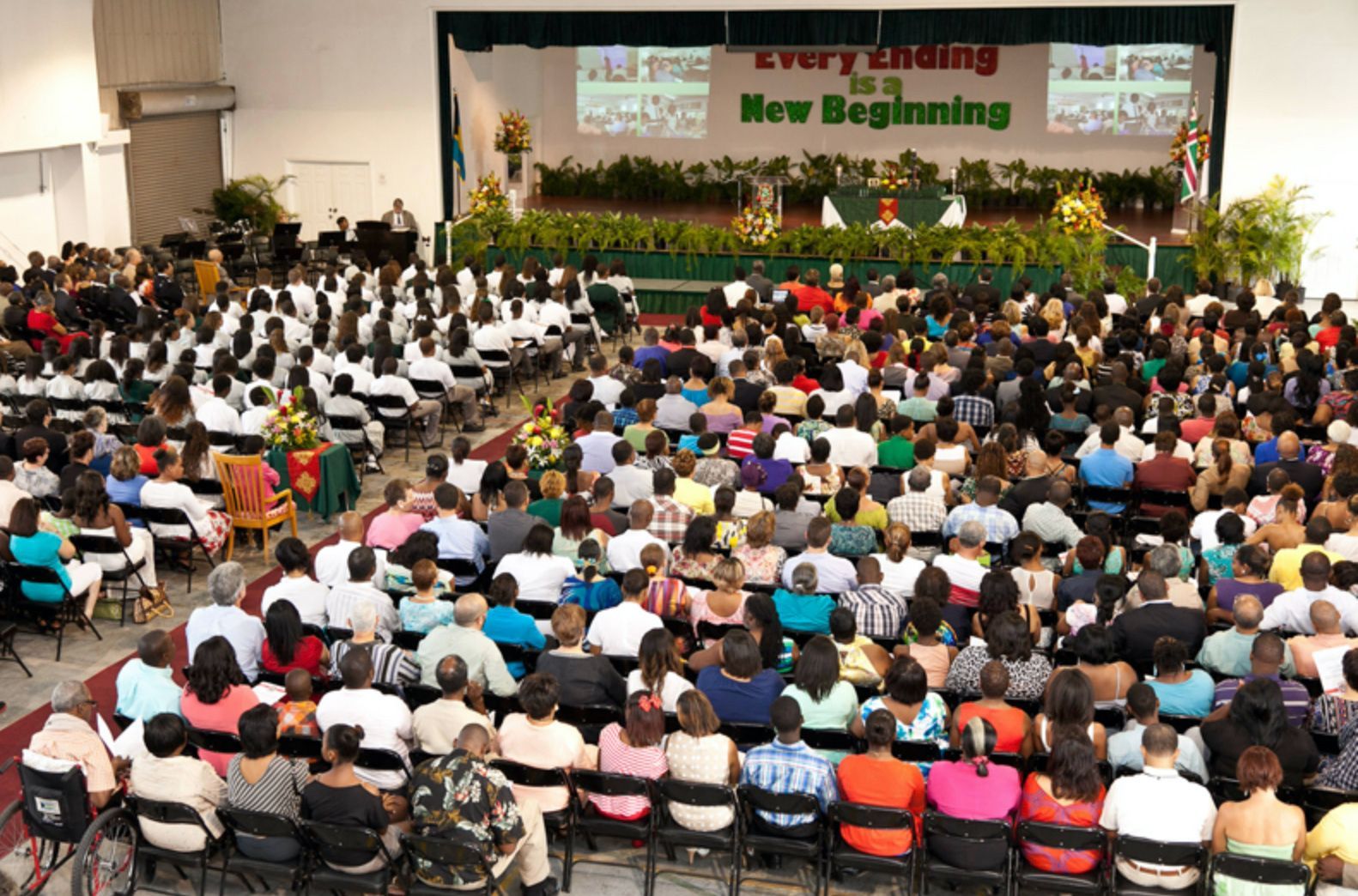 A large crowd of people sitting in front of a stage that says every ending new beginning