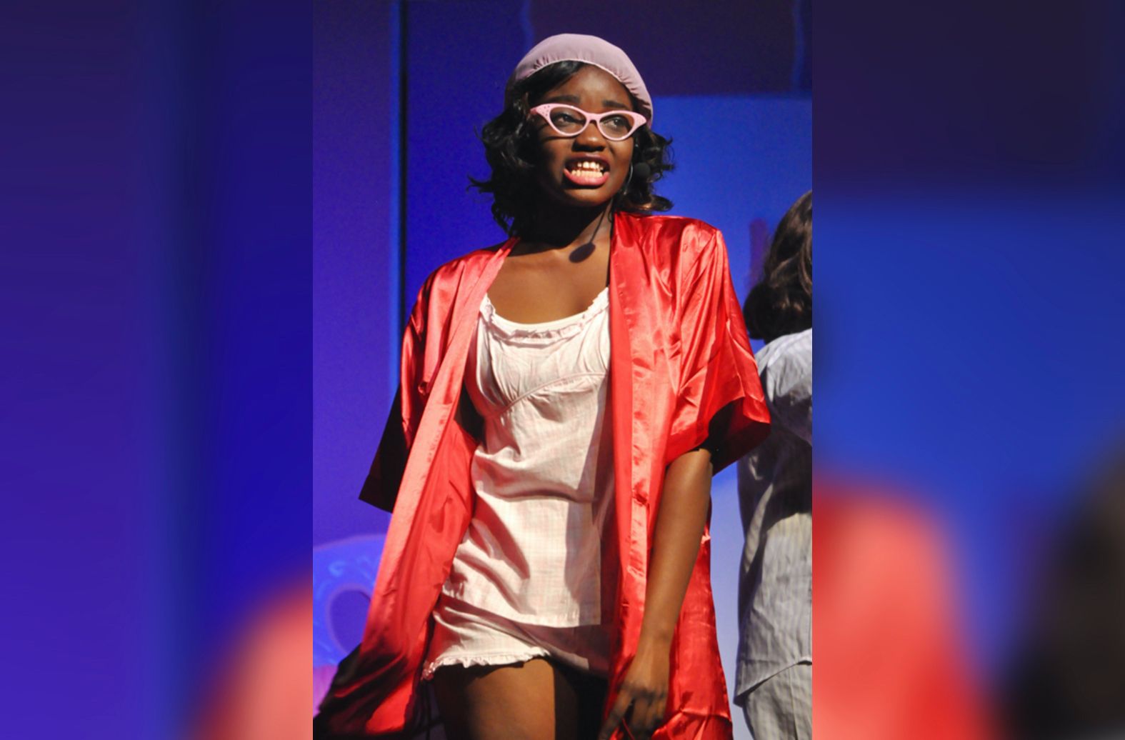 A woman wearing glasses and a red robe stands on a stage