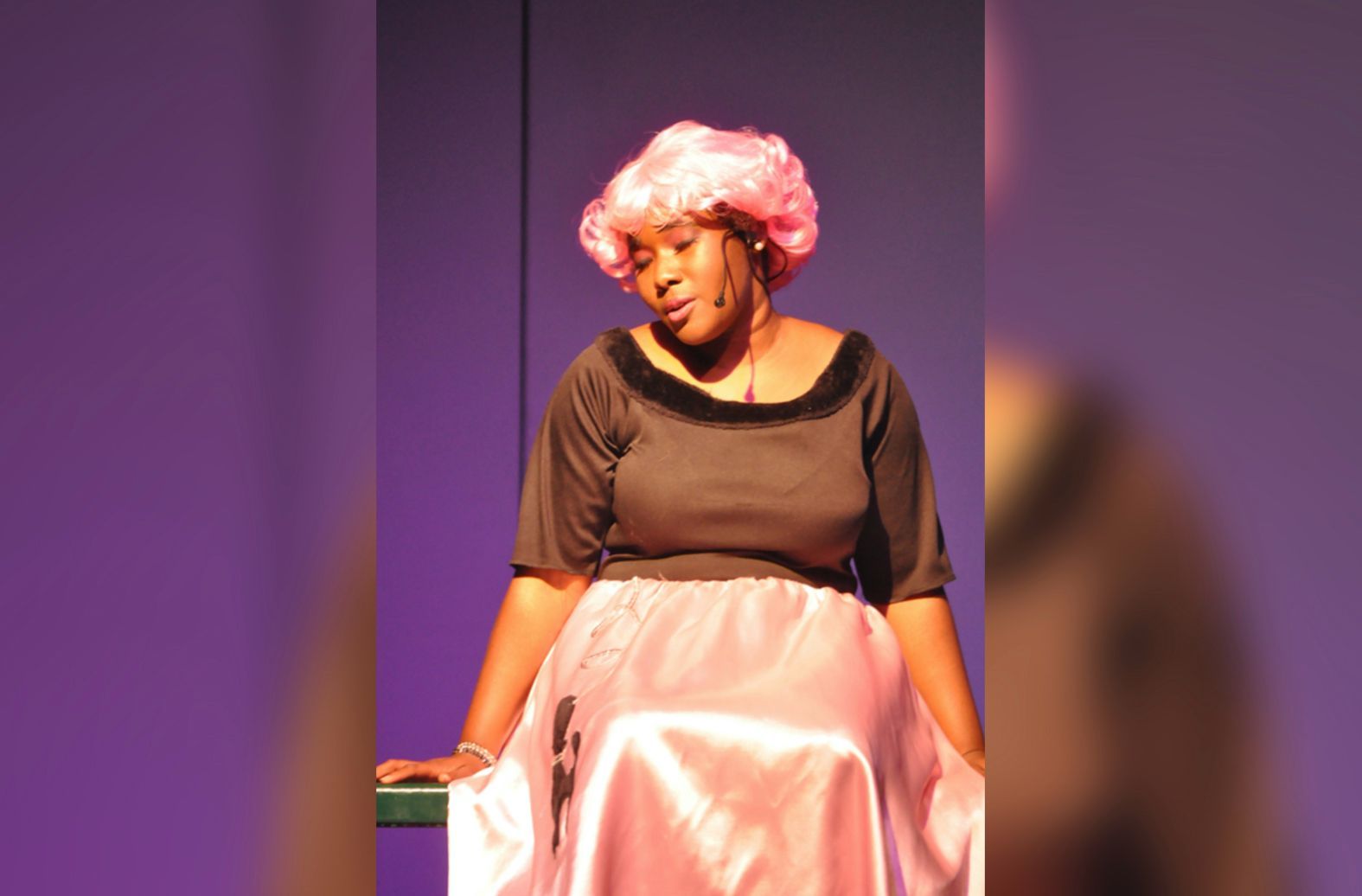 A woman wearing a pink wig sits on a bench