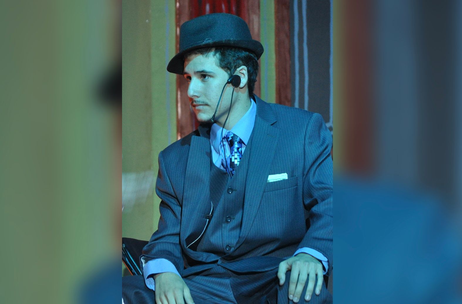 A man in a suit and hat is talking on a phone