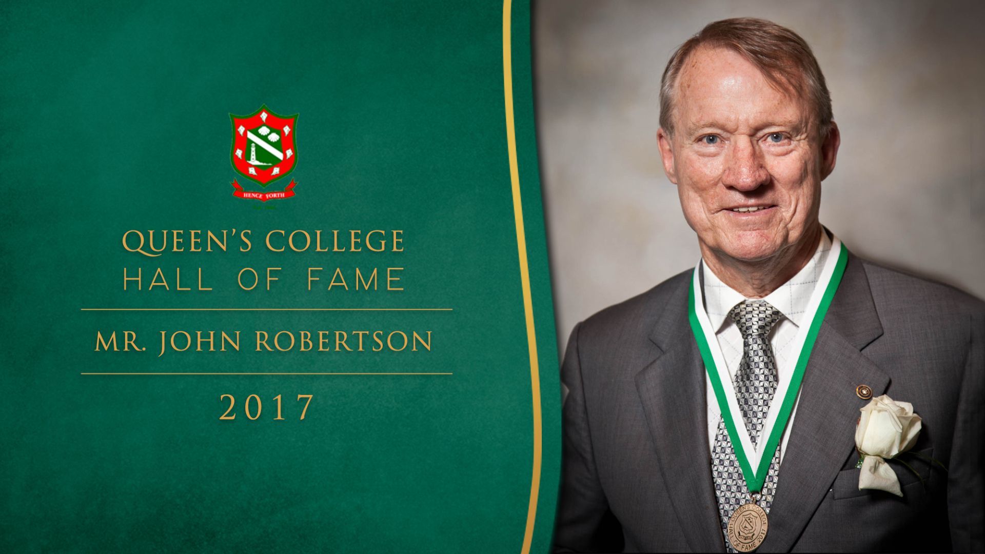 A man in a suit and tie is standing in front of a green sign that says queen 's college hall of fame