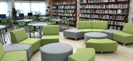 There are a lot of green chairs and tables in the library.