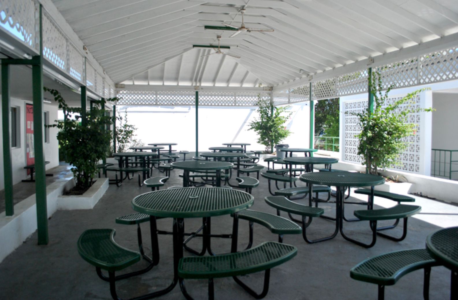 A picnic area with green tables and benches under a white roof
