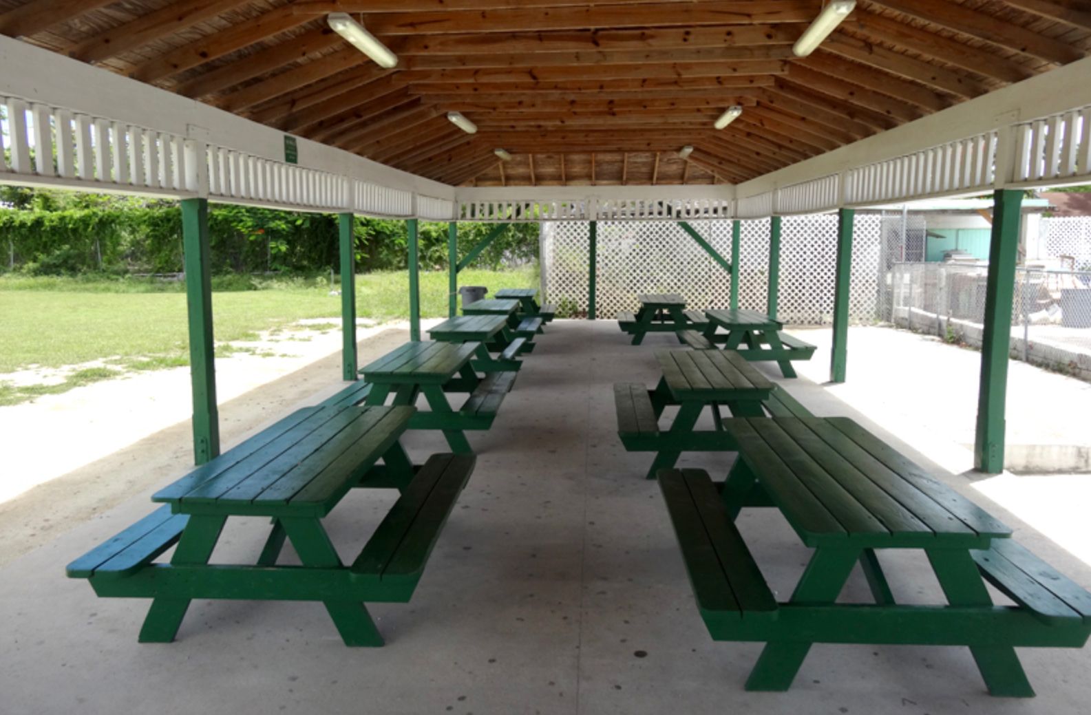 A row of green picnic tables under a wooden roof