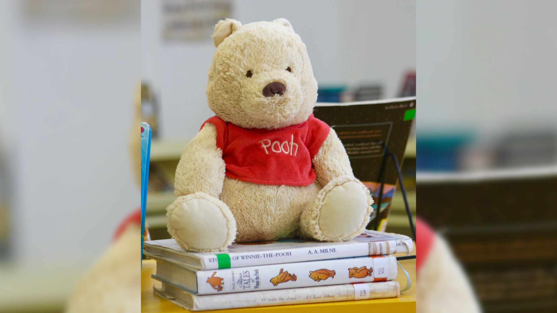 A winnie the pooh teddy bear sits on top of a stack of books