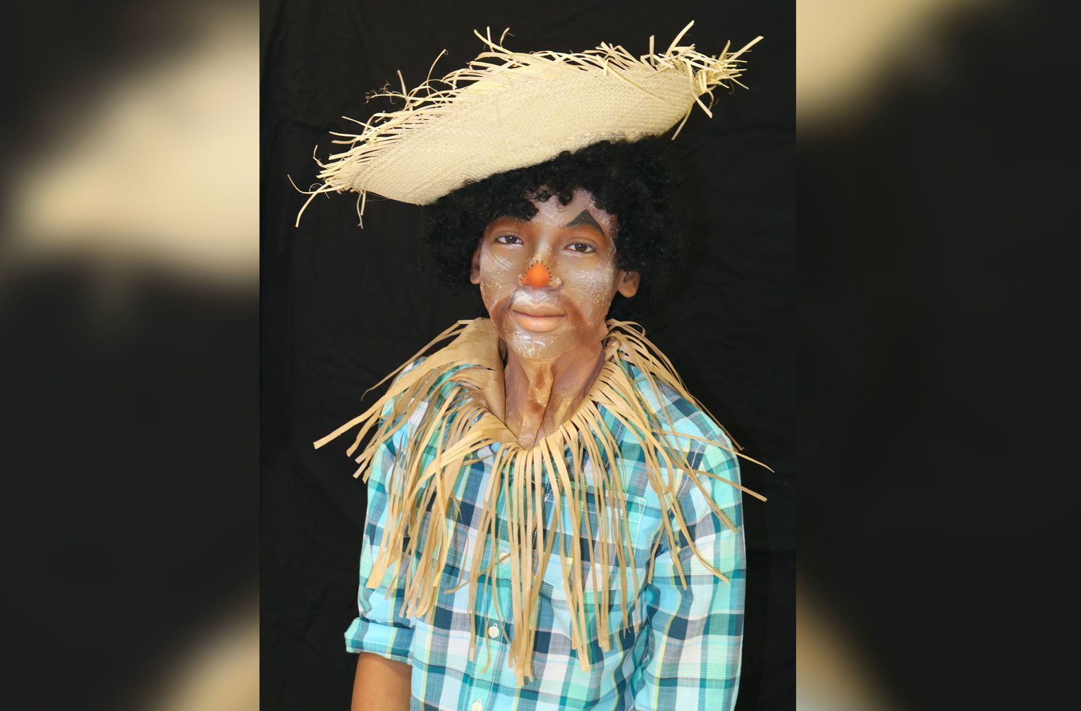 A young boy dressed as a scarecrow with a straw hat