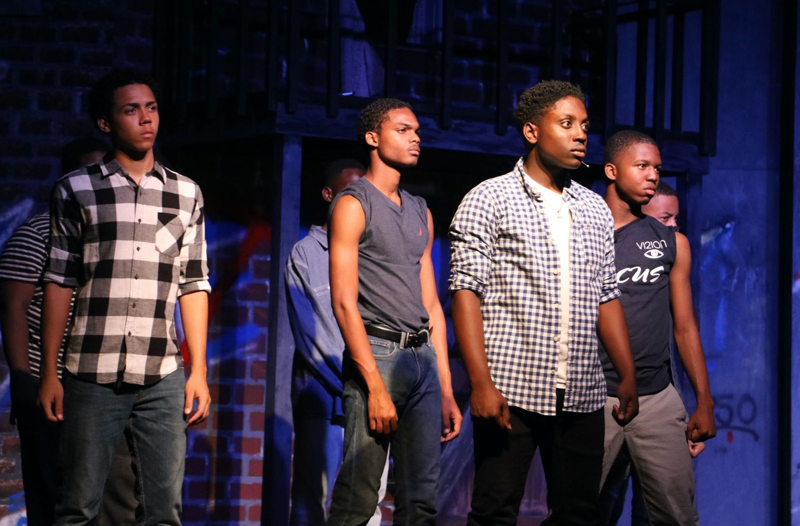 A group of young men are standing on a stage with one wearing a shirt that says ' a ' on it