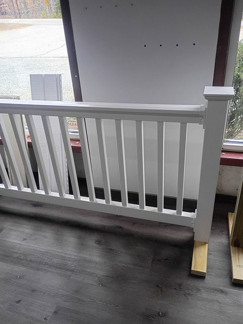 White railing beside a gray rooftop walkway and building wall, with a support post and nearby window.