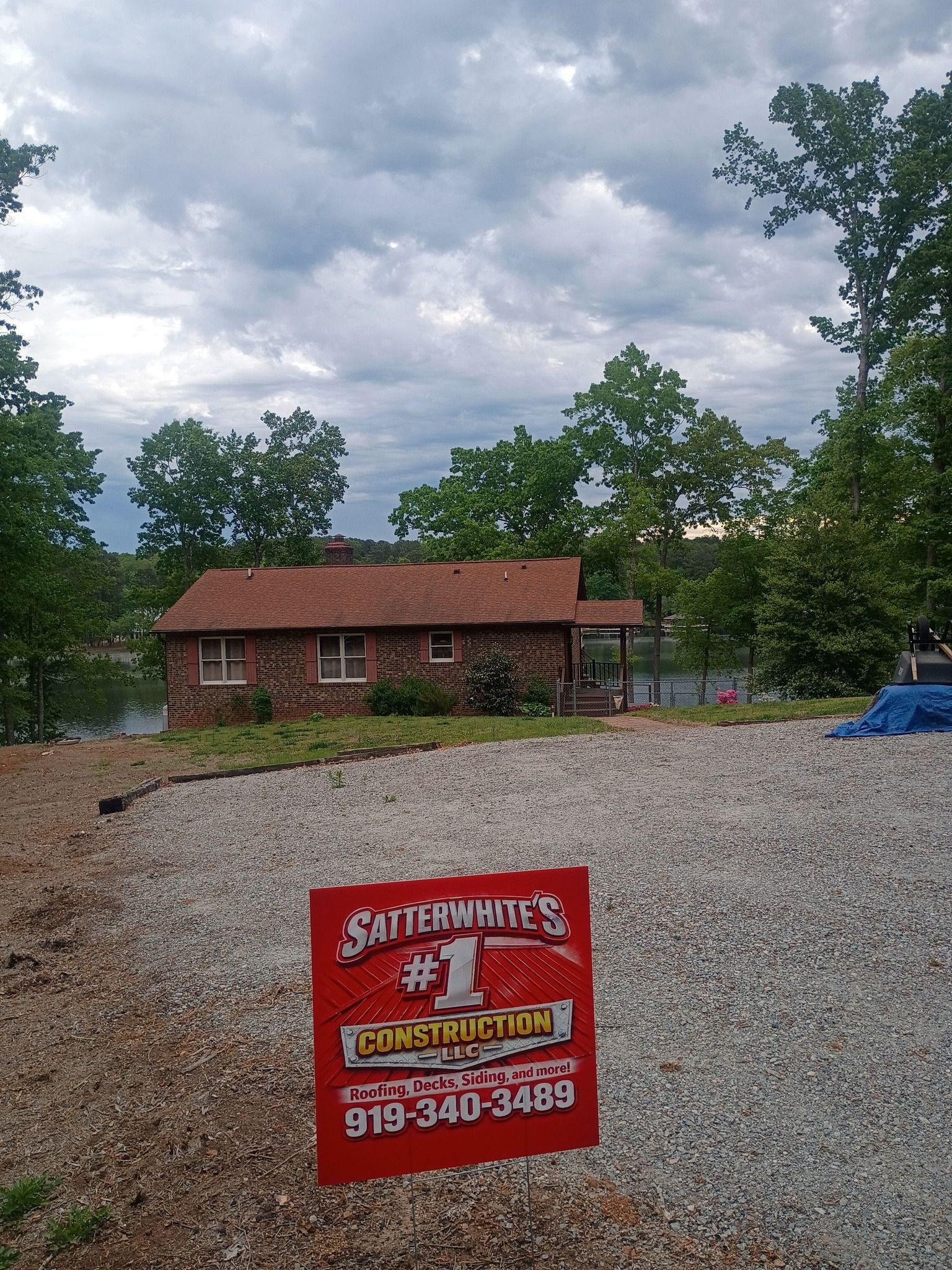 Red sign in gravel yard before a small brick house under cloudy sky