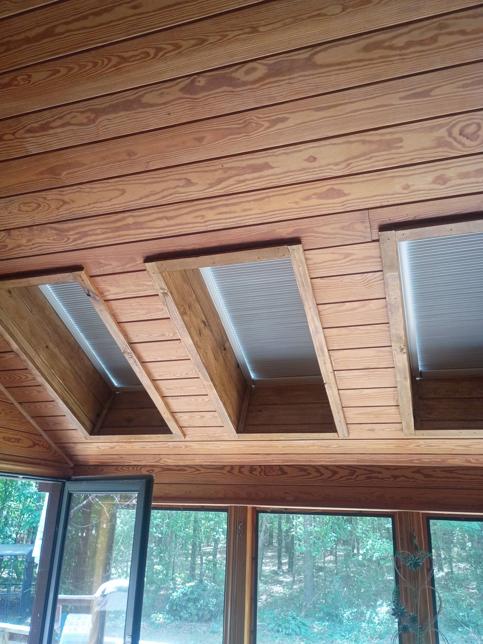 Wooden ceiling with three skylight panels above large windows in a bright sunroom