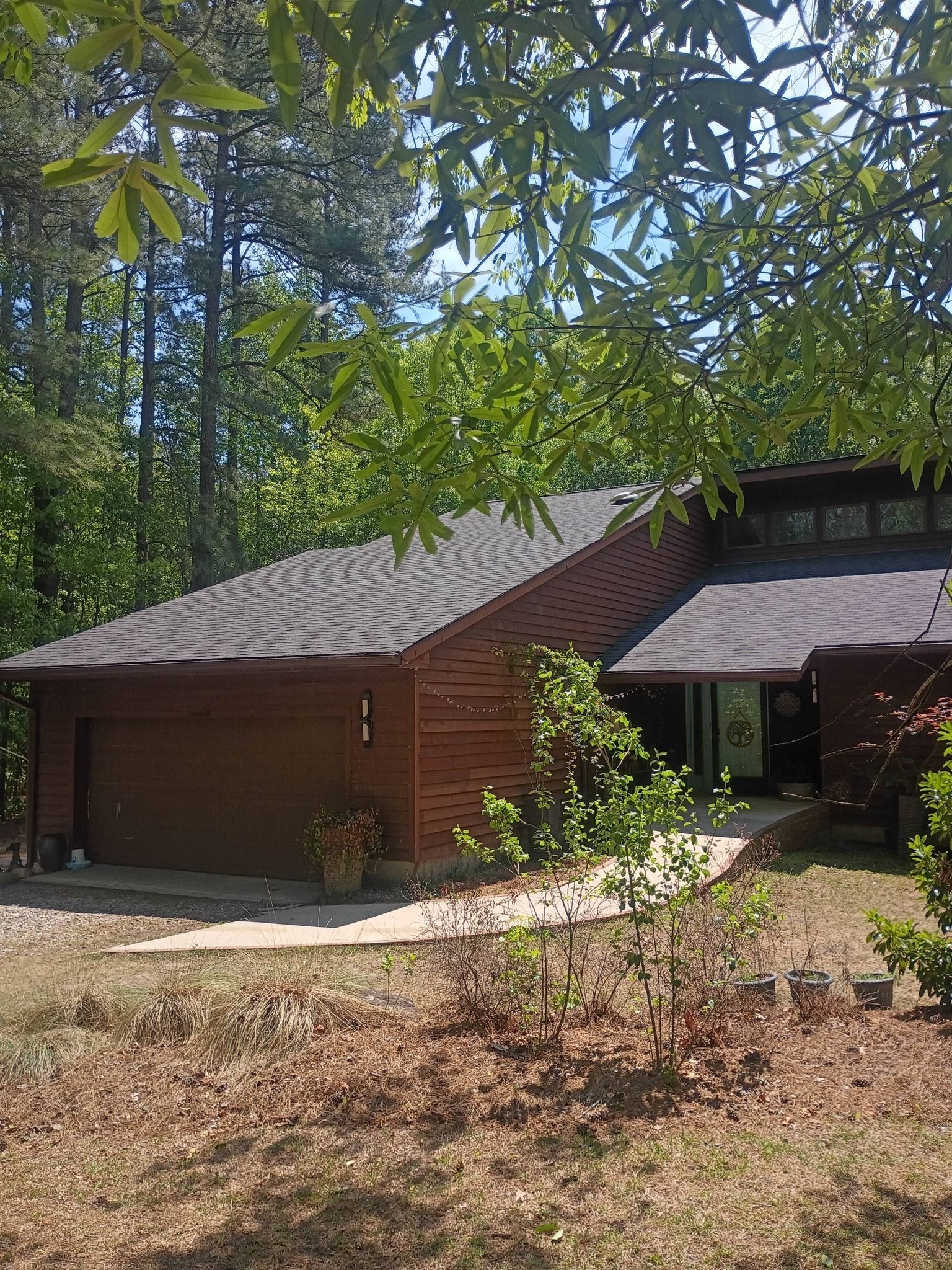 Brown wooden cabin in a wooded area with a shingled roof and a shaded porch