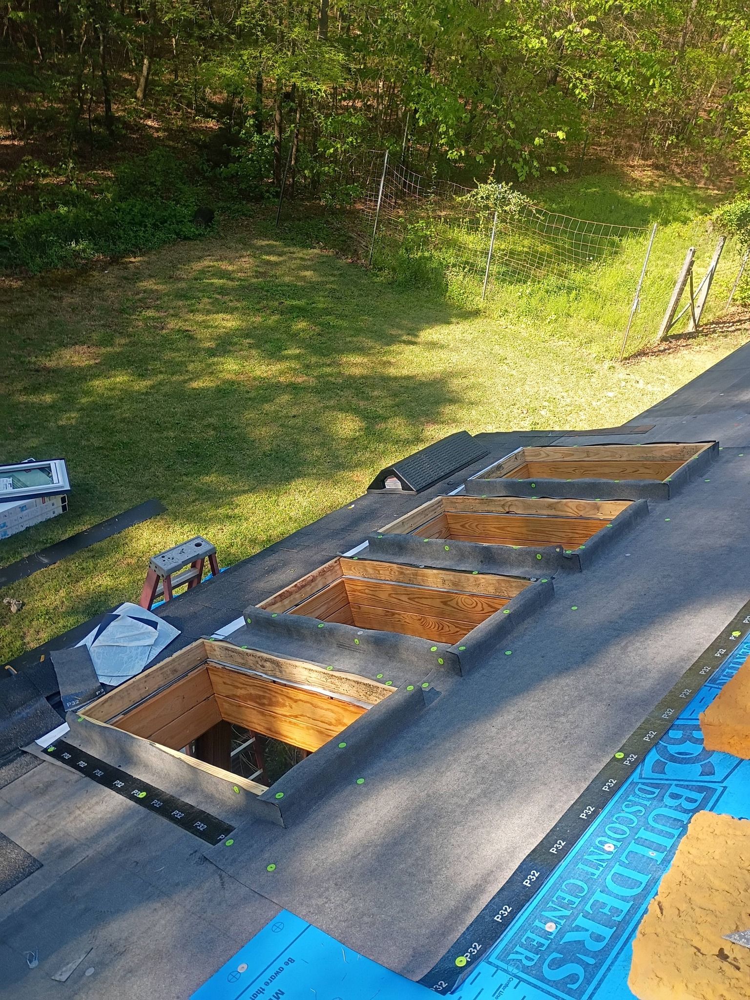 Rectangular raised garden bed frame with wooden compartments on a rooftop or patio beside grass and trees