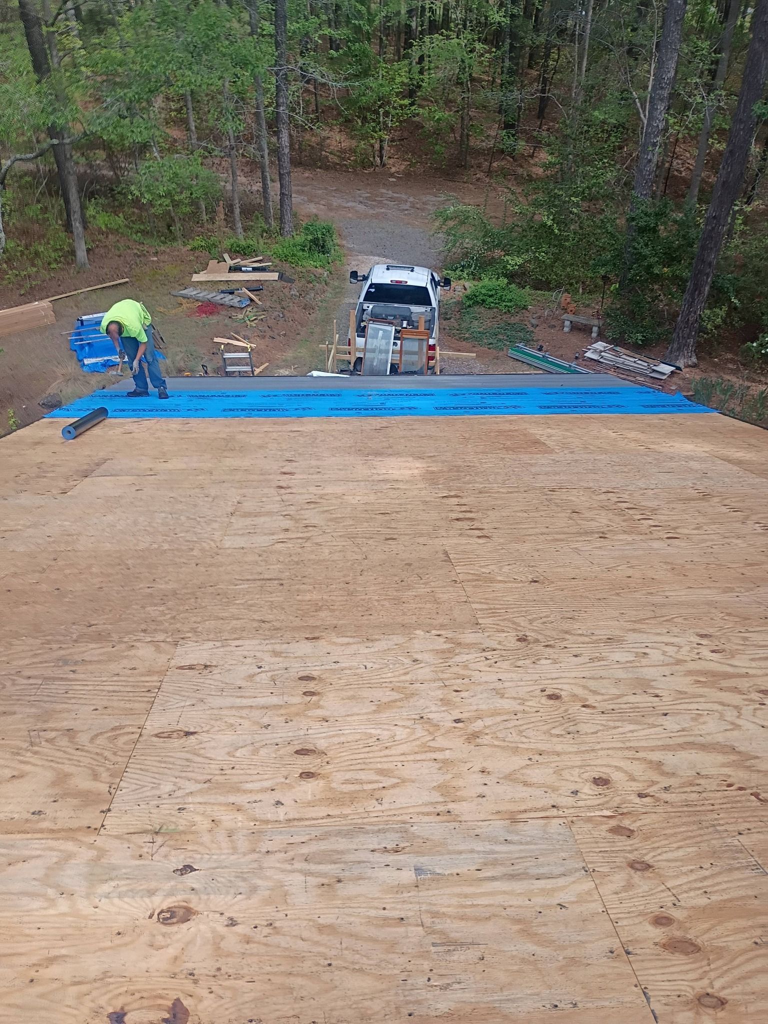 Construction workers installing a blue tarp on a dirt slope beside a wooded yard and parked truck