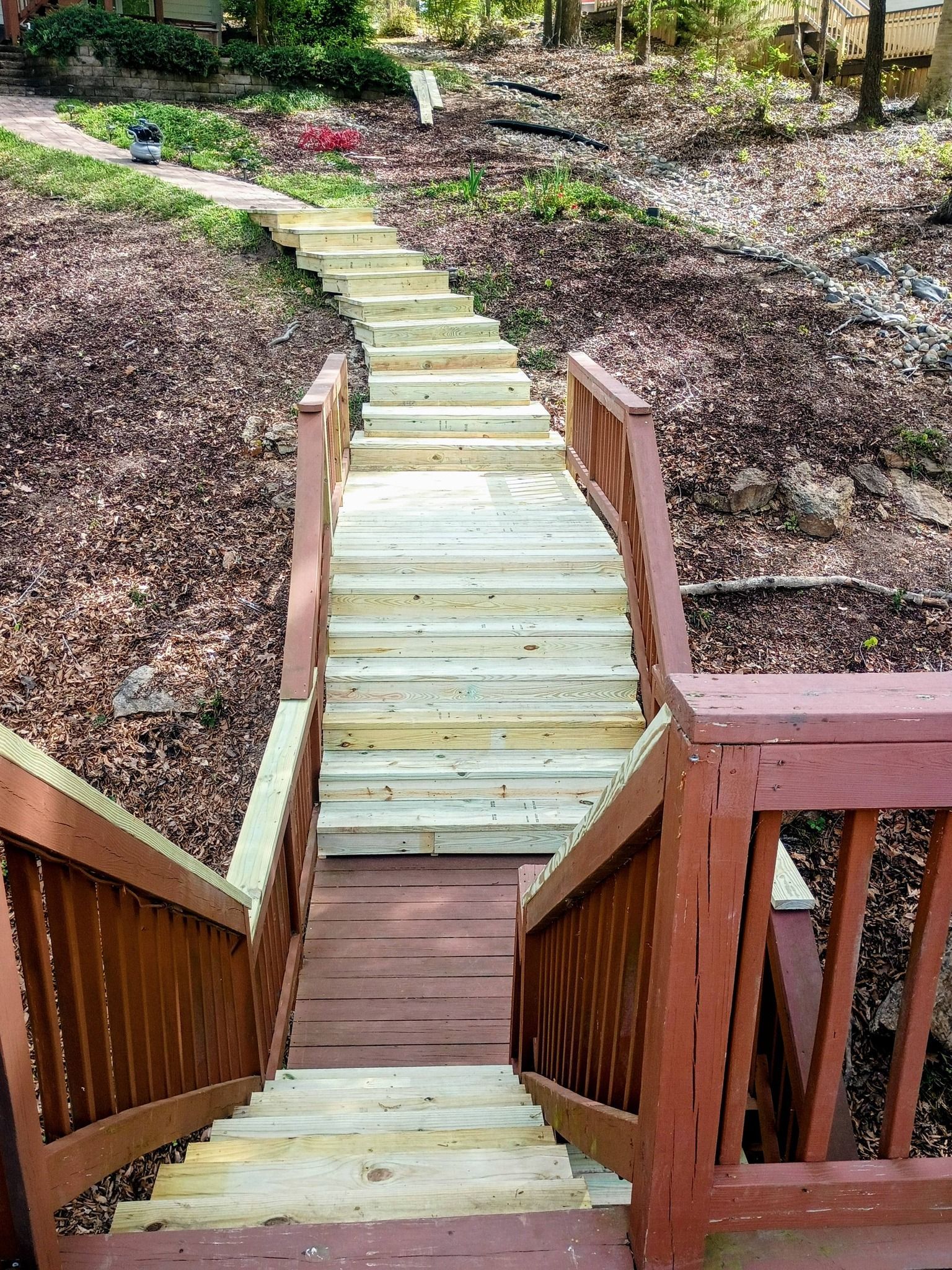 Wooden stairs and walkway descending a landscaped garden path with mulch and greenery on both sides