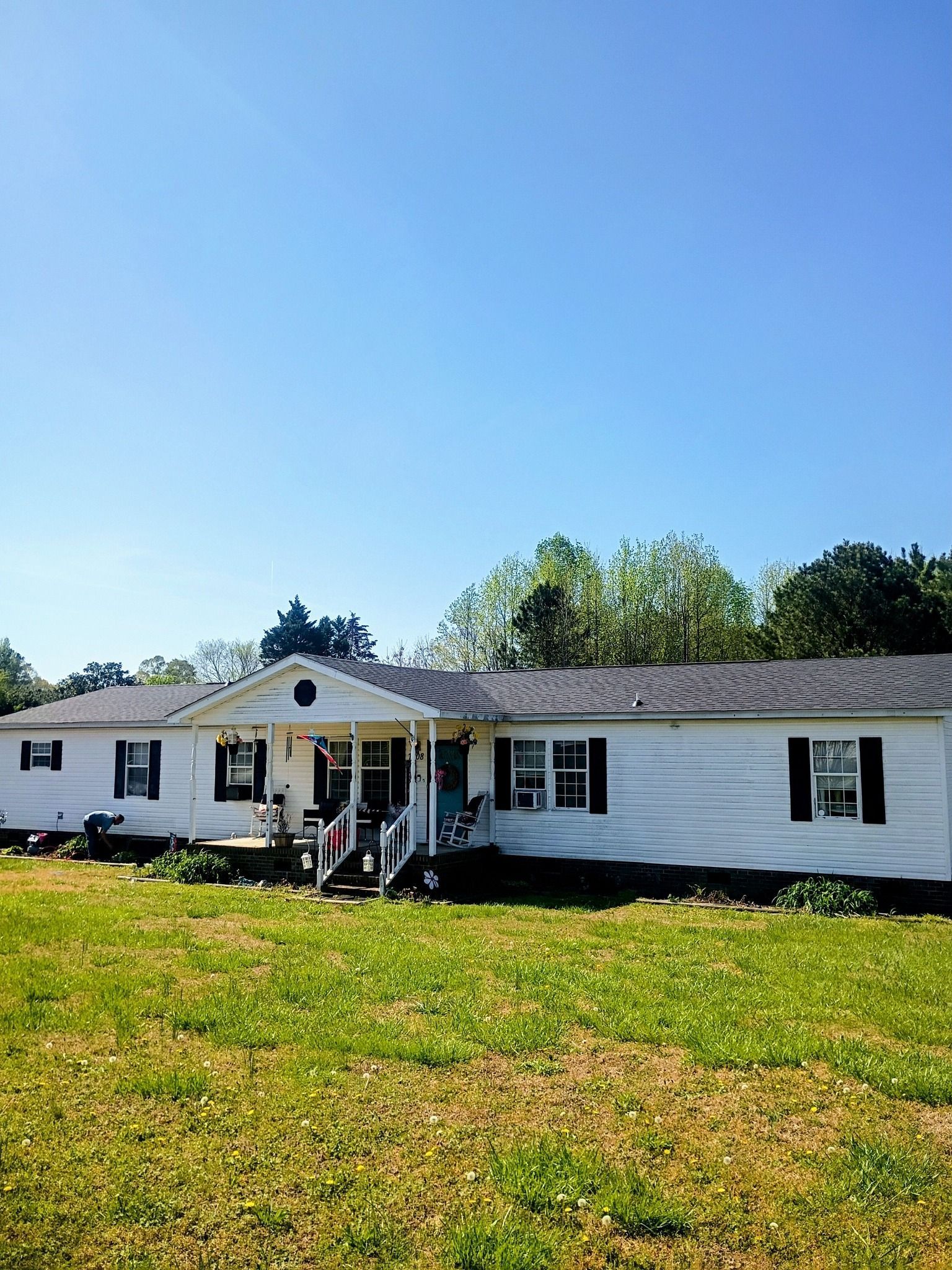 Single-story white house with black shutters, front porch, and green lawn under a bright blue sky