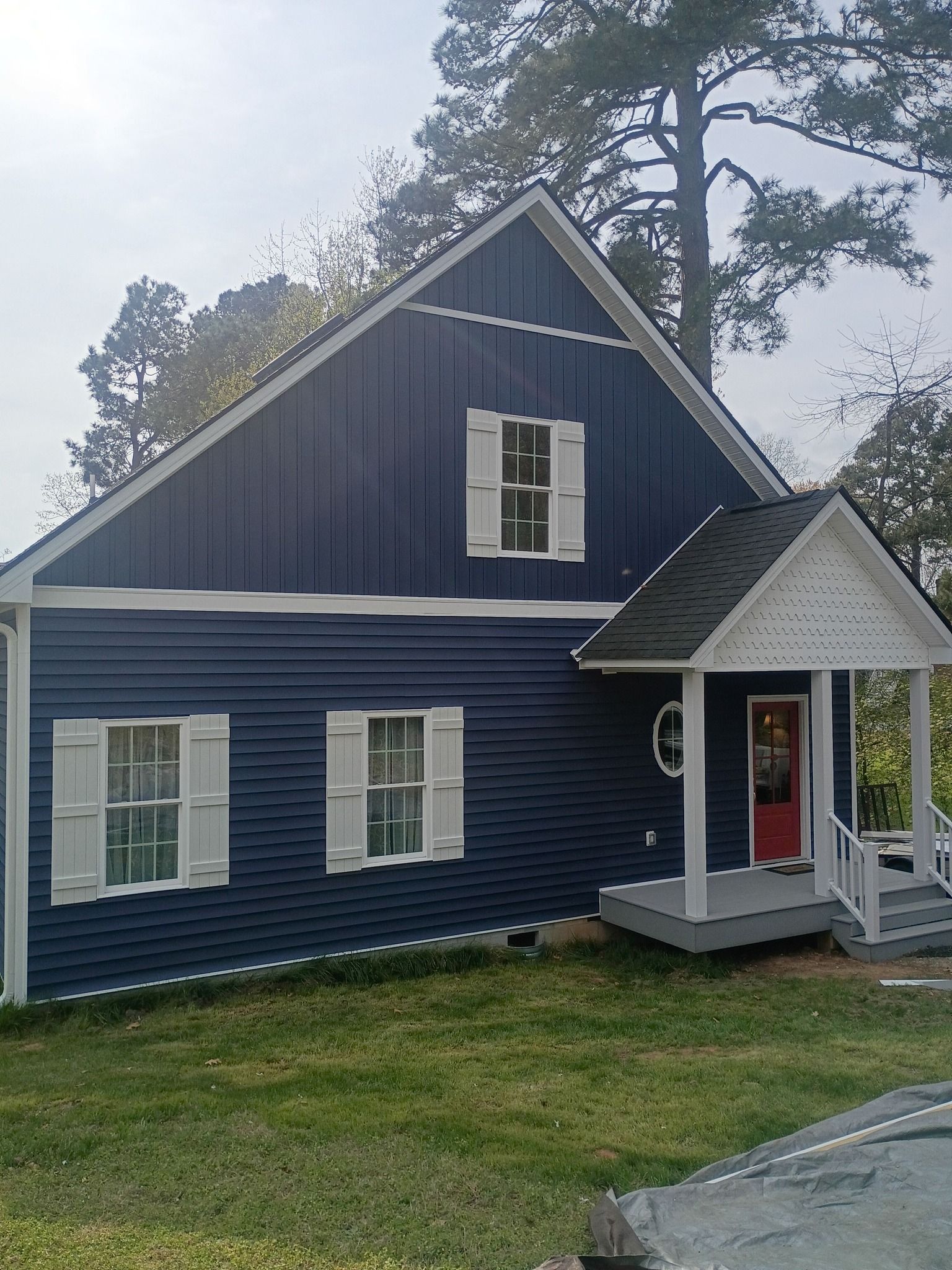 Blue two-story house with white trim and front porch, set on a grassy lot with trees around it.