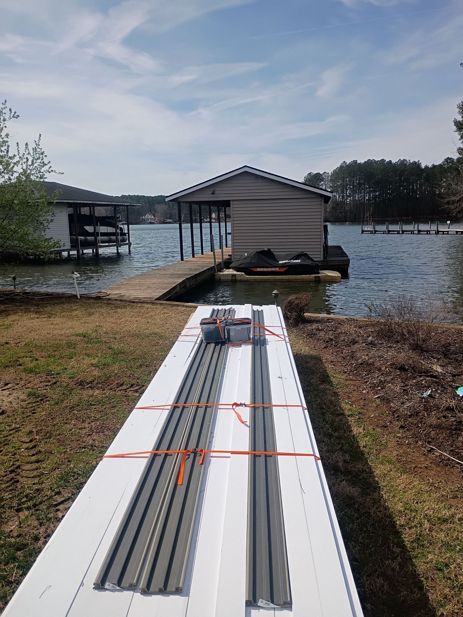 White kayak dock ramp leading to a boathouse on a calm lake under a partly cloudy sky