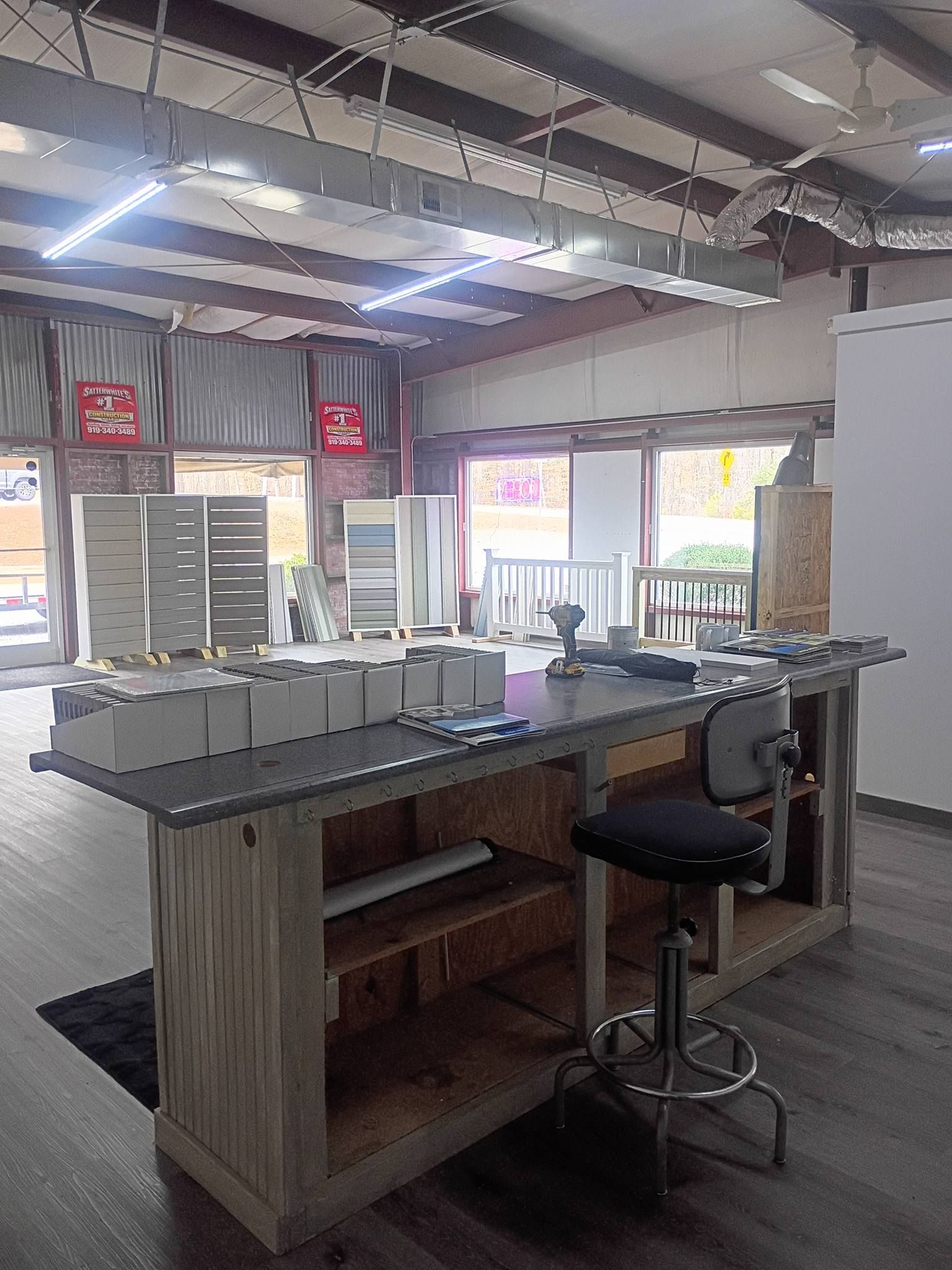 Bright open office interior with a standing desk, stool, shelving, and large windows displaying signs