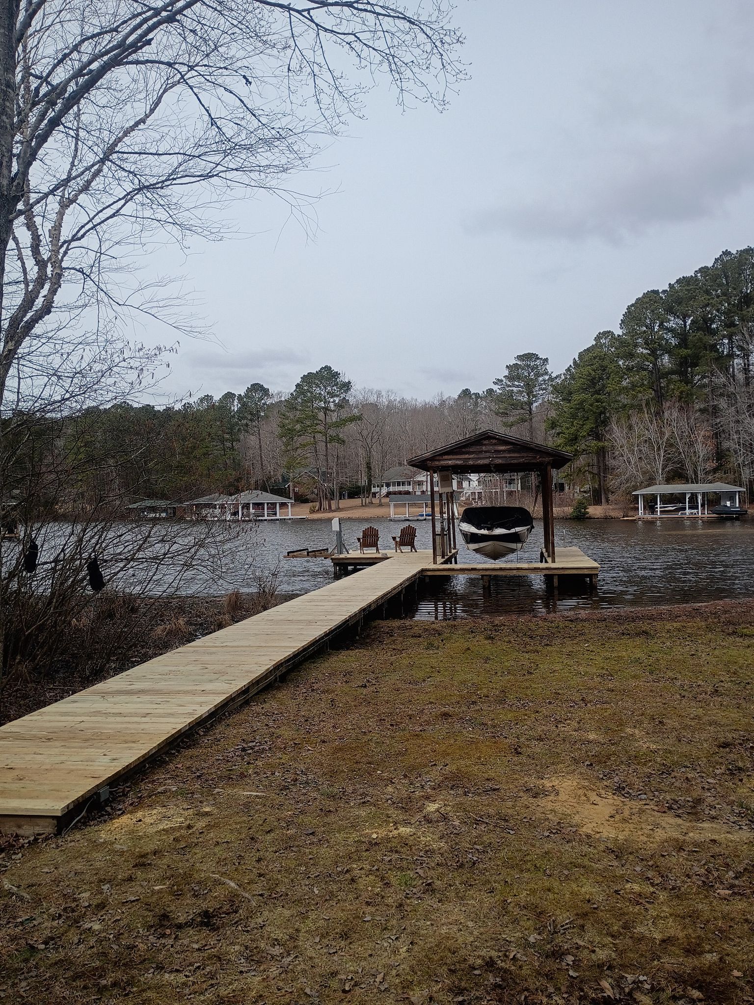 Wooden dock leading to a lakeside gazebo on a cloudy day, surrounded by bare trees and water.