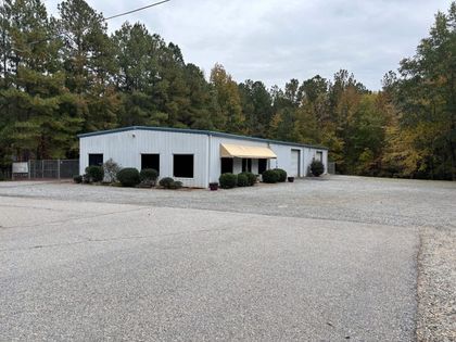 White metal building with a small awning, surrounded by a large gravel lot and trees.