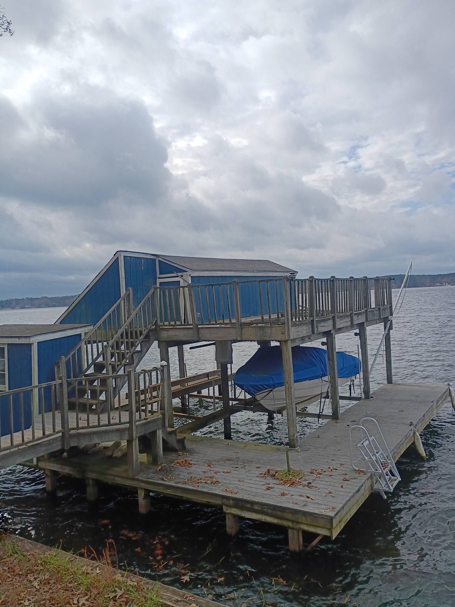 Blue docked boat beside a weathered wooden pier on choppy water under a cloudy sky
