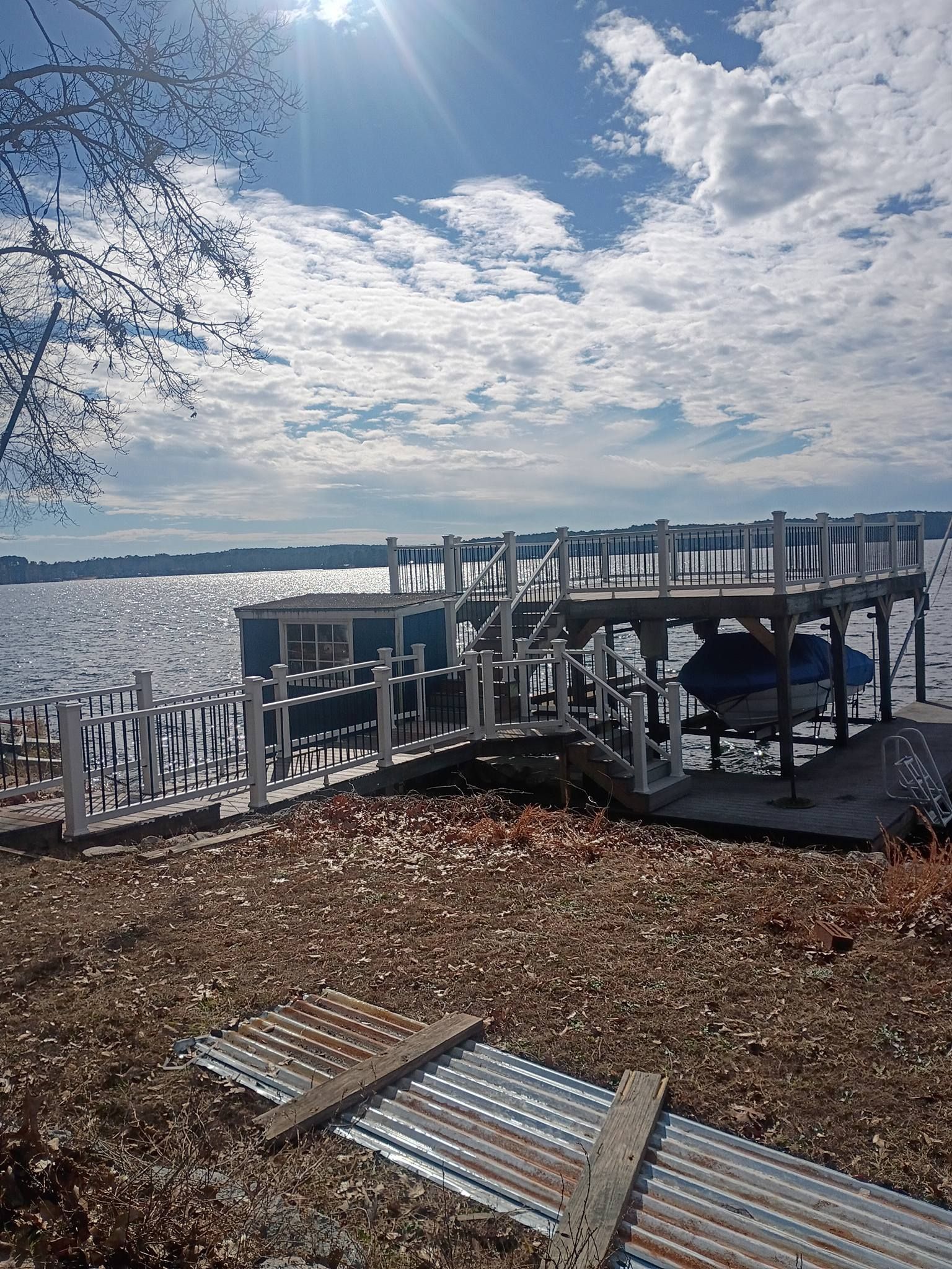 Snow-dusted lakeside dock with railings and a cloudy sky over open water, with fallen leaves in the foreground