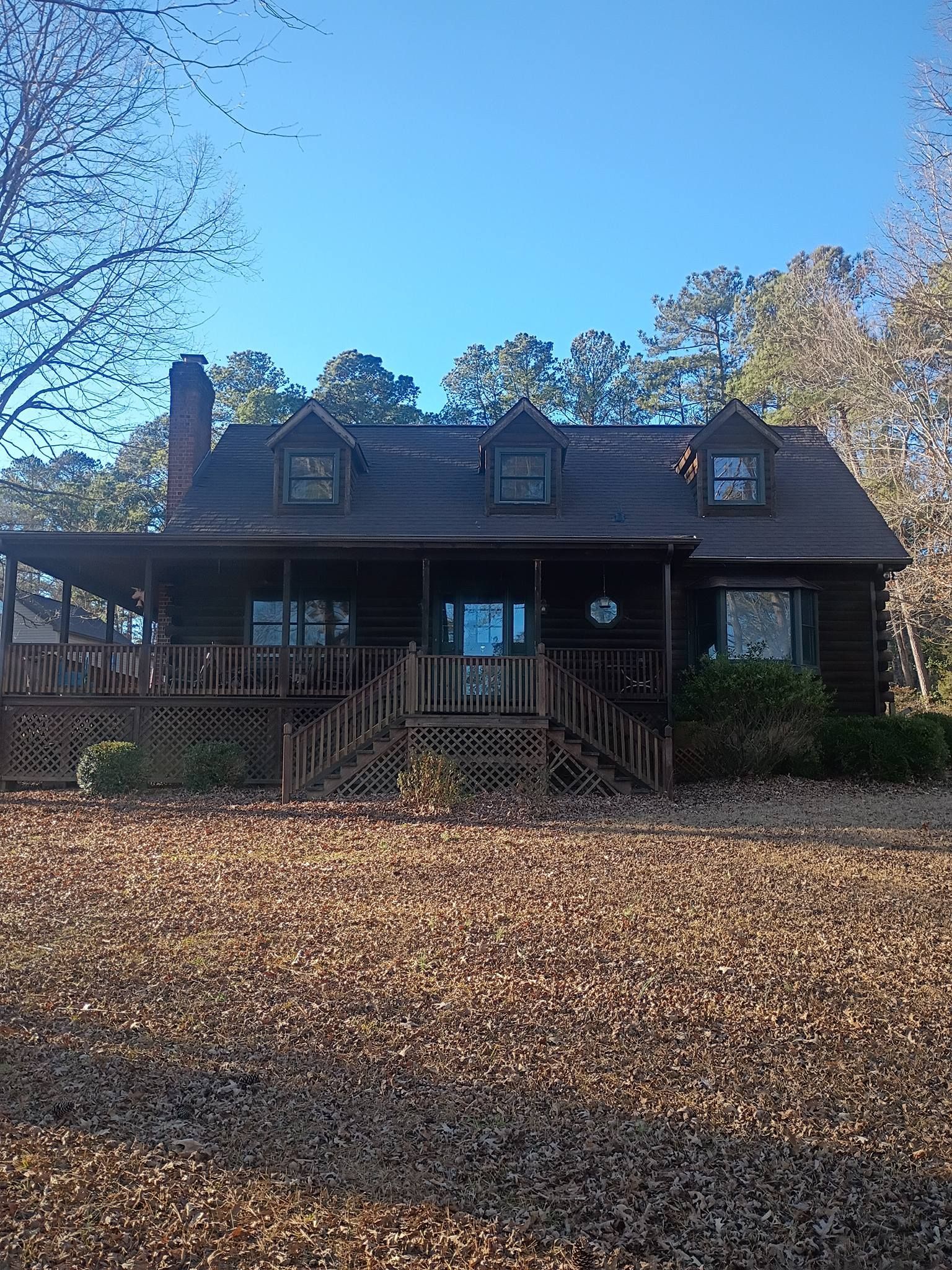 Wooden cabin with porch and dormer windows, framed by autumn leaves under a blue sky.