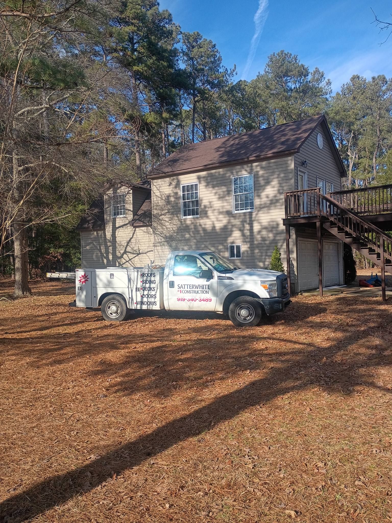 White utility truck parked by a stone house in a wooded yard with fallen leaves.