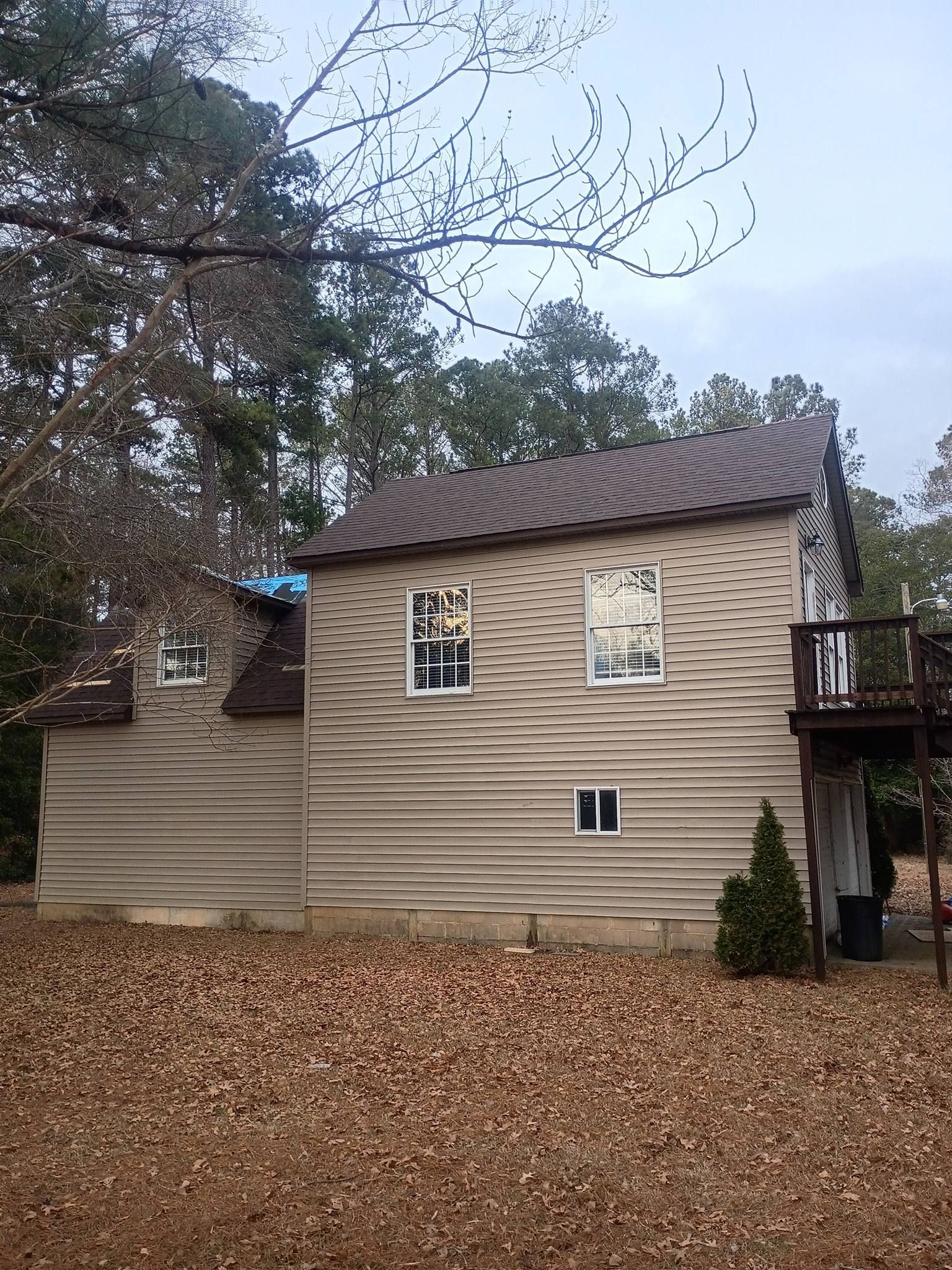 Beige house with brown roof and deck, surrounded by fallen leaves and trees in autumn