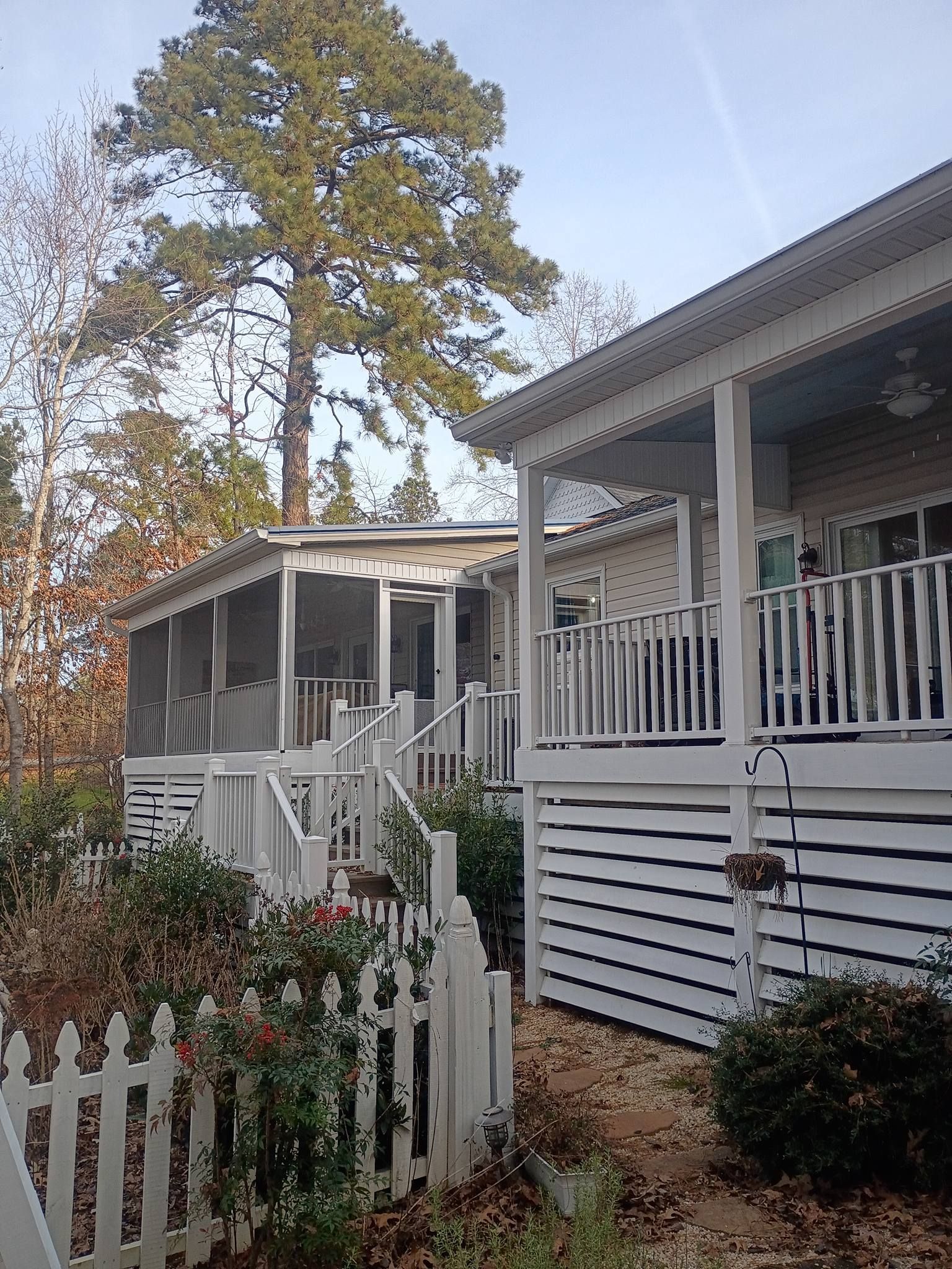 White porch-lined houses with railings and a picket fence in a leafy yard