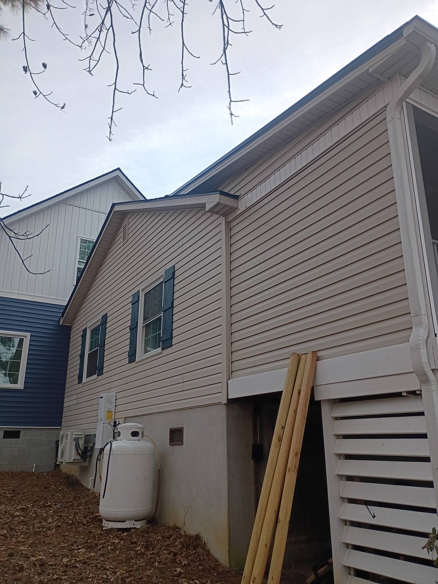 Side view of beige house with blue-trimmed windows, white siding, and a propane tank beside the foundation.
