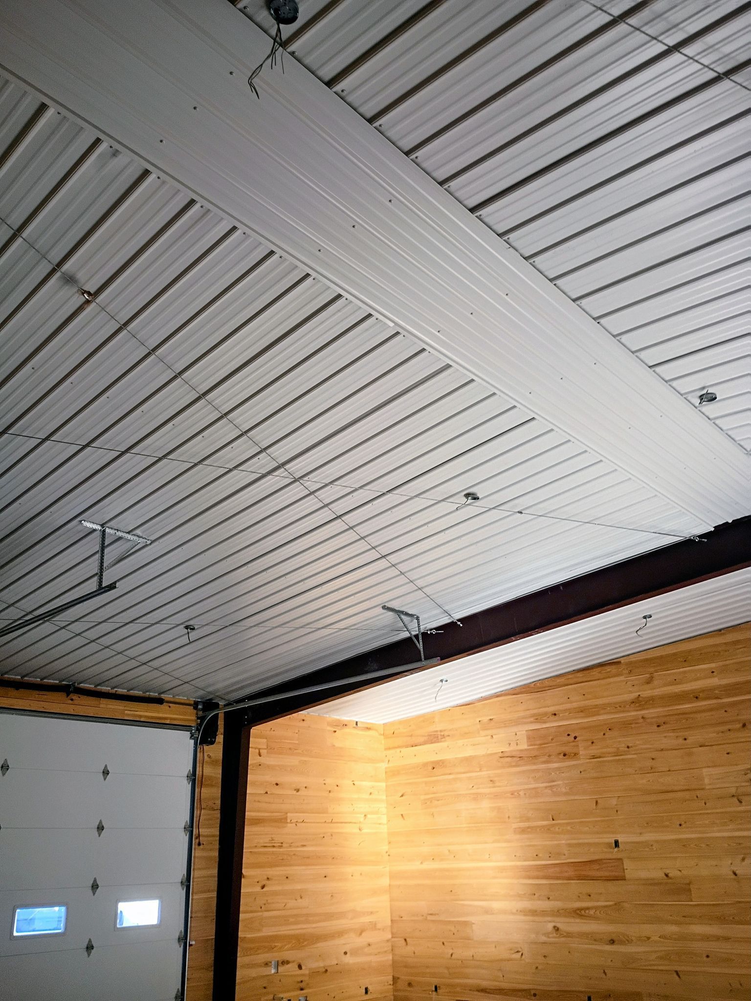 Interior with white slatted ceiling, gray garage-style door, and wooden wall panels in a corner.