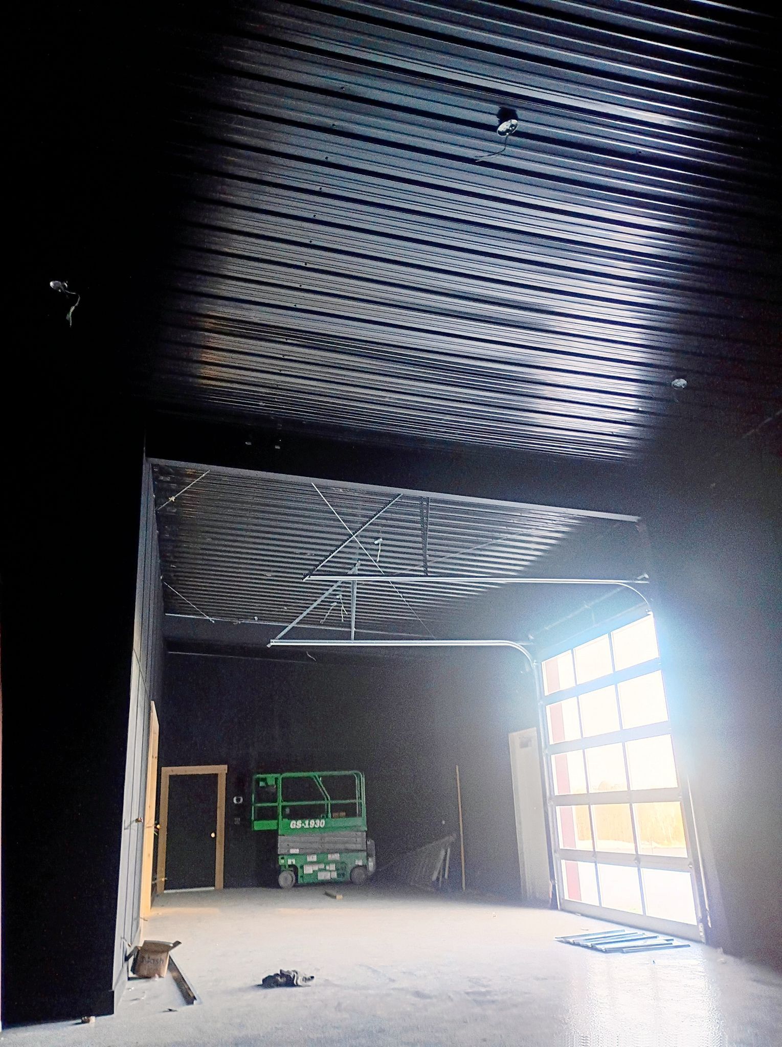 Empty industrial room with dark ribbed ceiling, green machine at back, and bright open doorway on the right