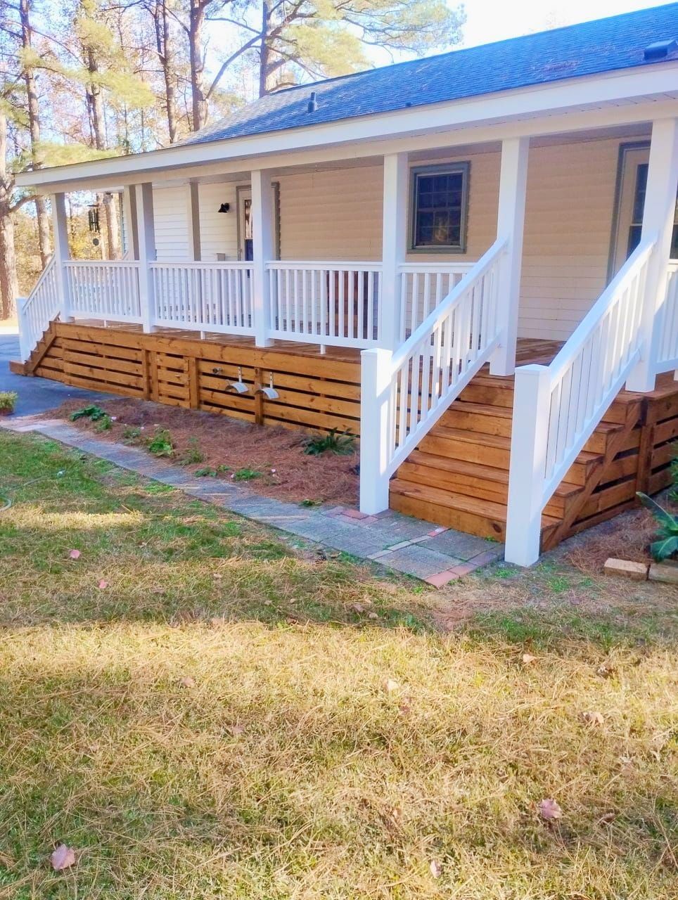 Front porch with white railings and steps on a beige house, with wood lattice skirting and a grassy yard.