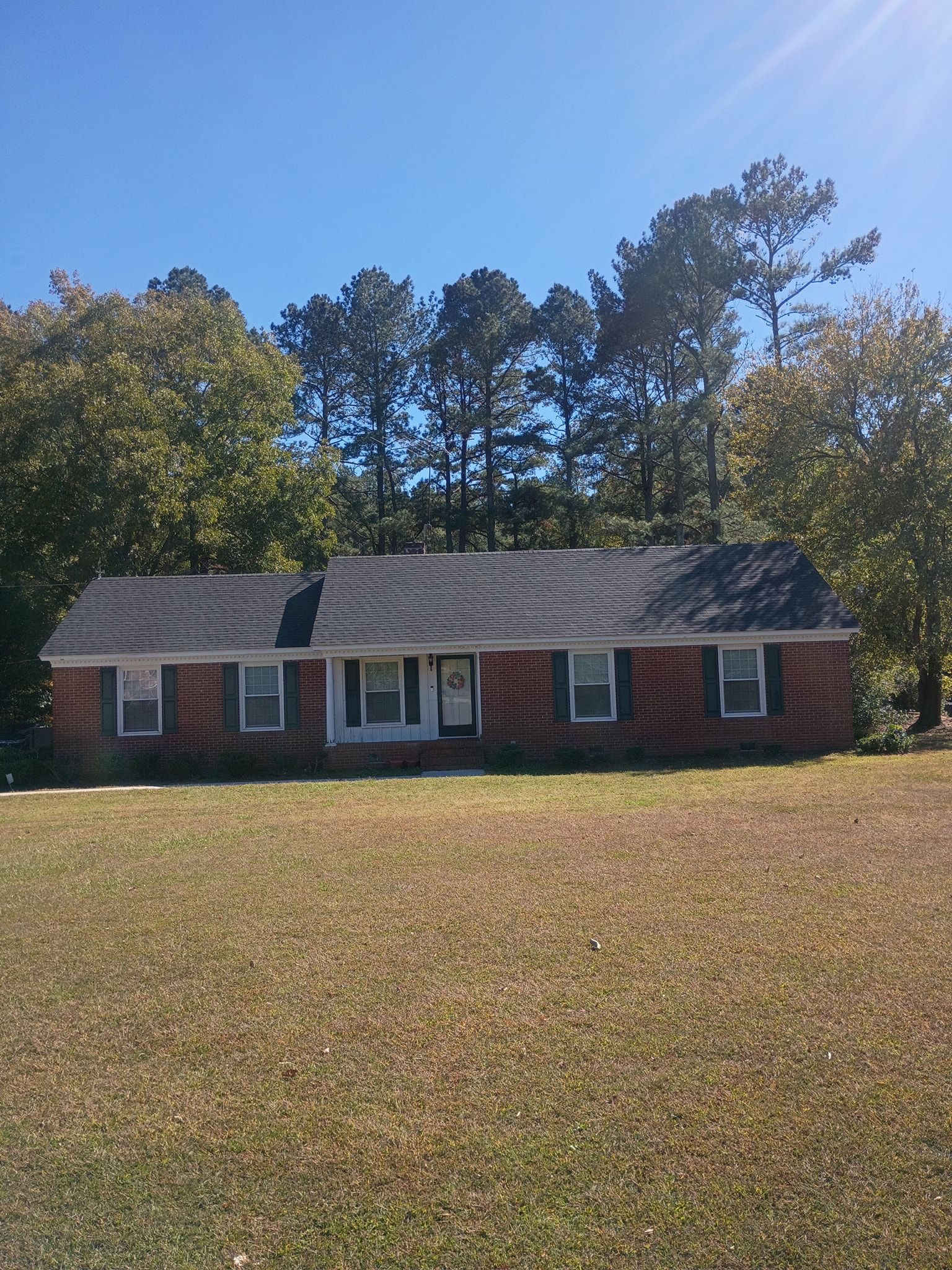 Single-story brick house with white trim and dark roof, surrounded by trees under a clear blue sky.